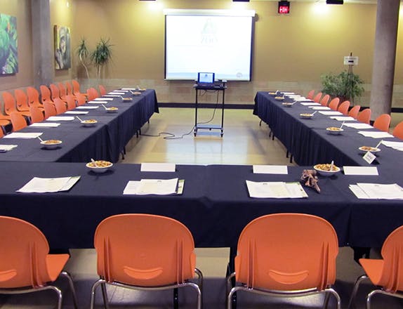 room set up with tables and chairs in a U-shape with screen and projector at the front.