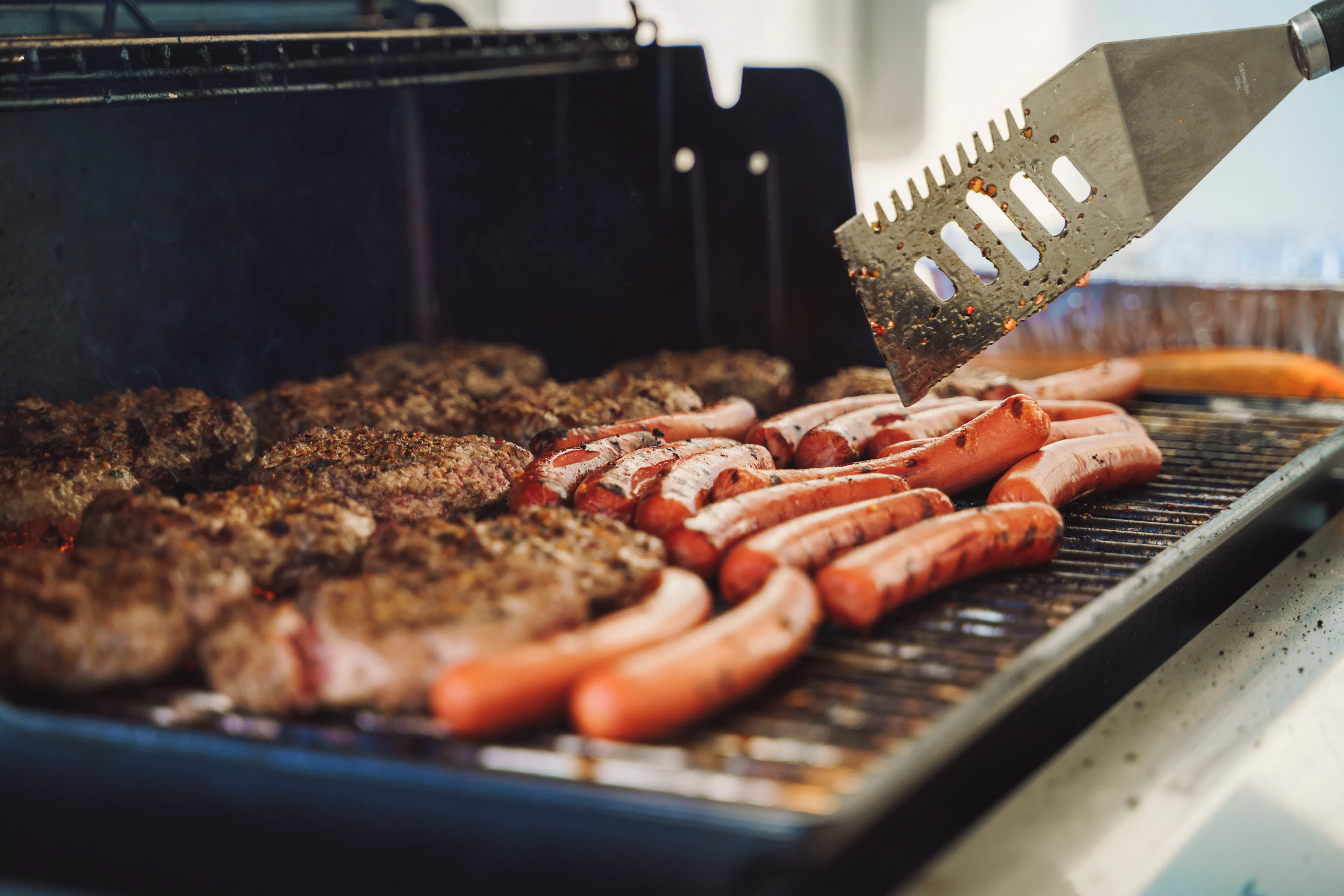 hot dogs and burgers cooking on grill
