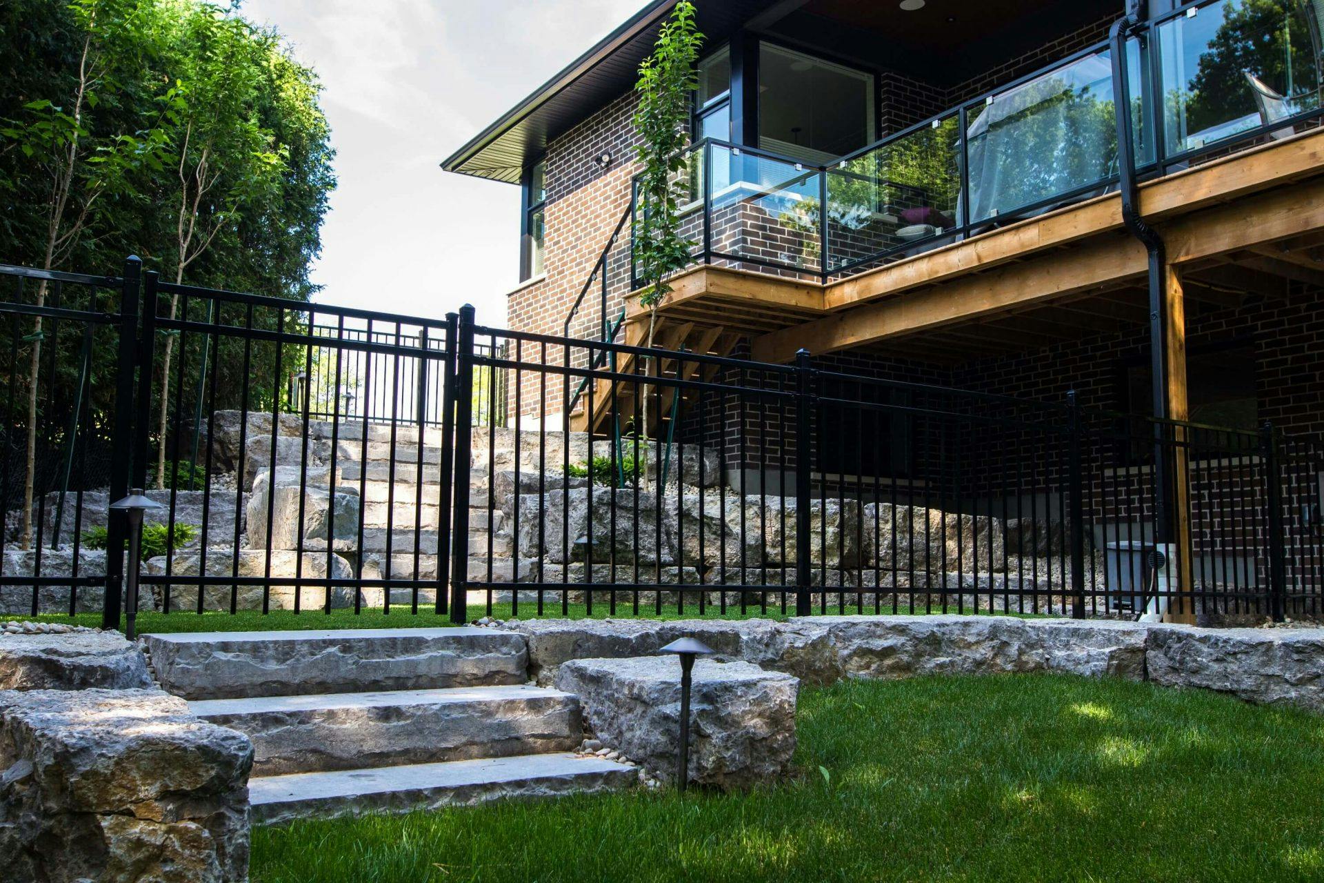 black iron spindled fencing partitioning backyard. Natural stone short wall and three stone steps at the base of the iron fence. 