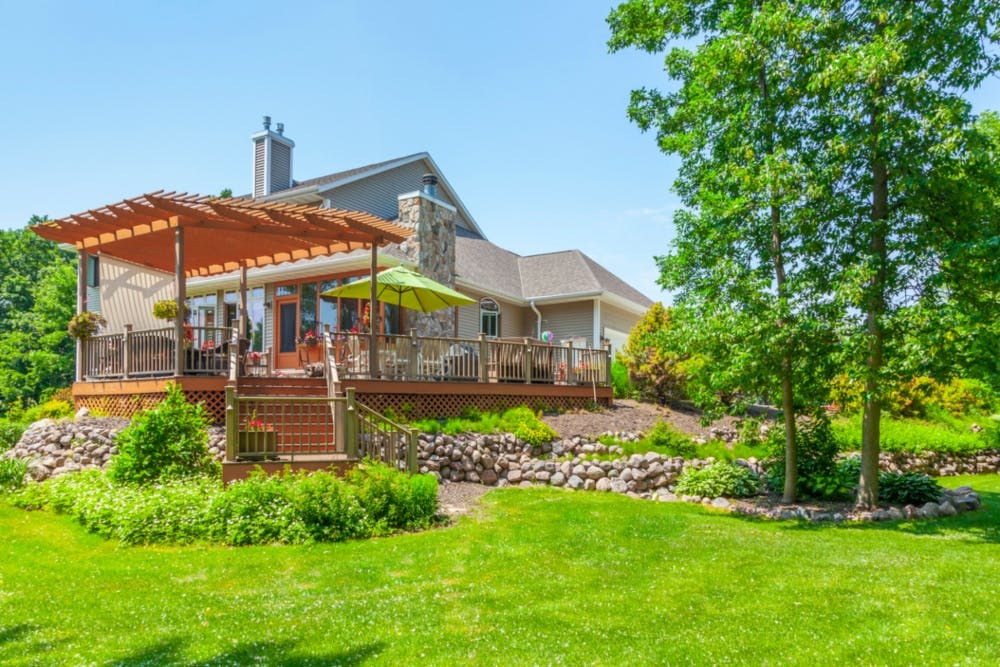 Gorgeous backyard on a bright sunny day featuring a deck and beautifully maintained garden and lawn with natural stone retaining walls.