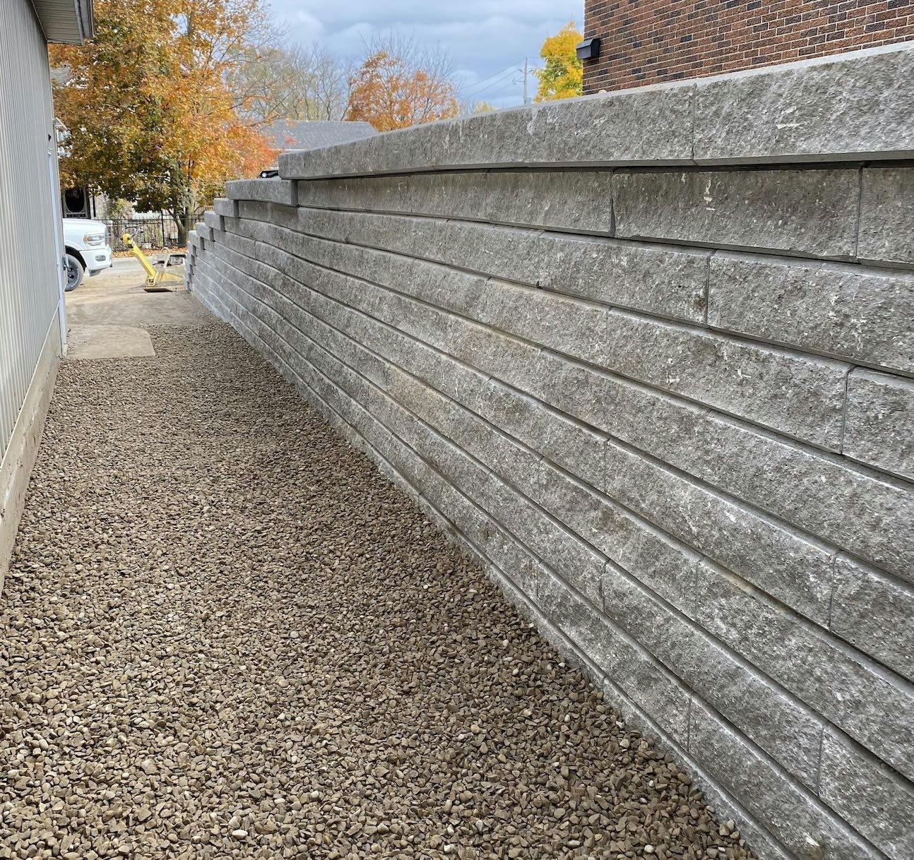 Beautiful grey four foot stone retaining wall separates two yards. One yard is at a higher elevation than the one next to it. The lower homes's side yard is lined with a nice pebbled rock treatment. 