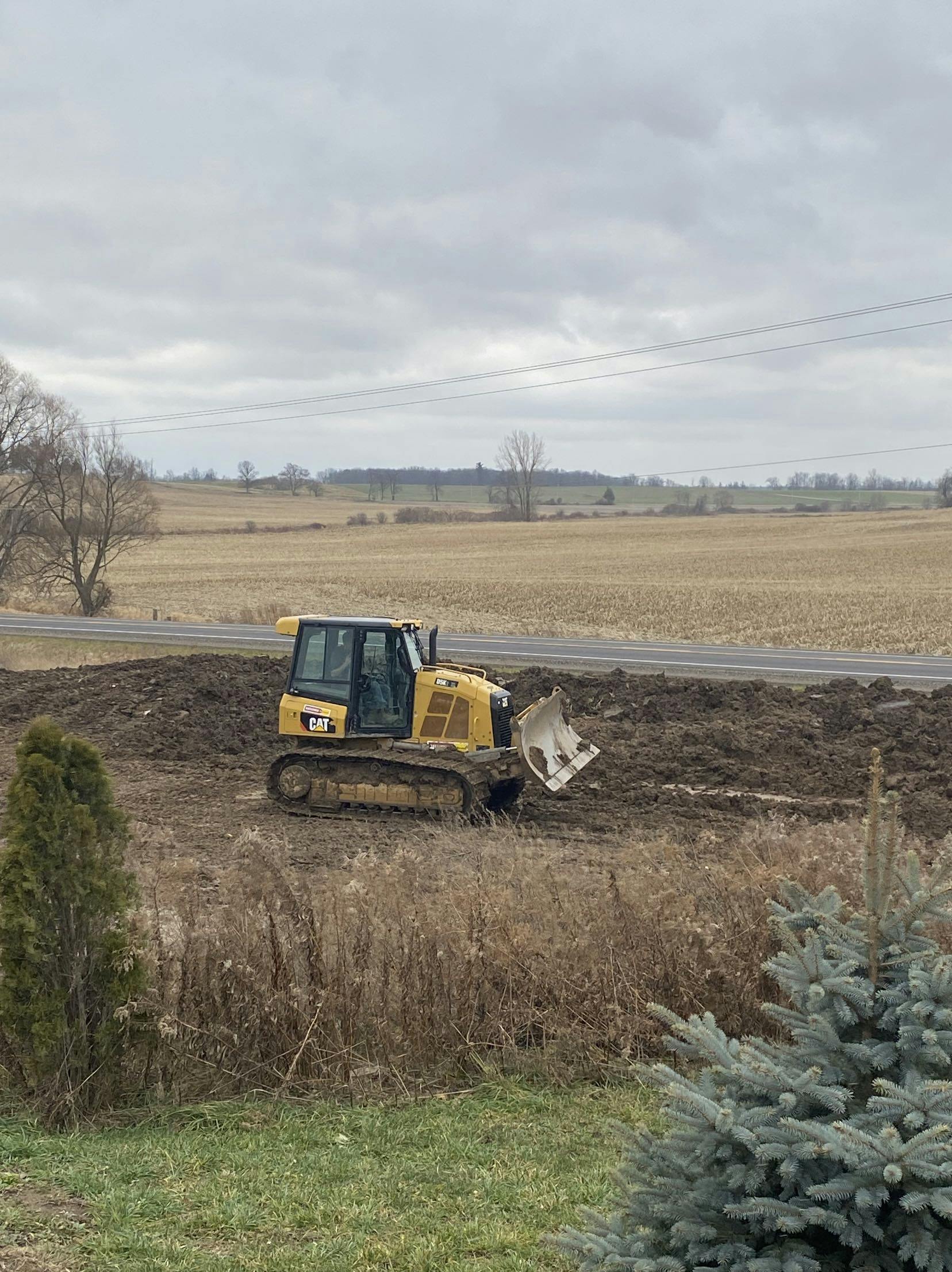 Bulldozer levels soil on the front yard of a home near a roadway. 