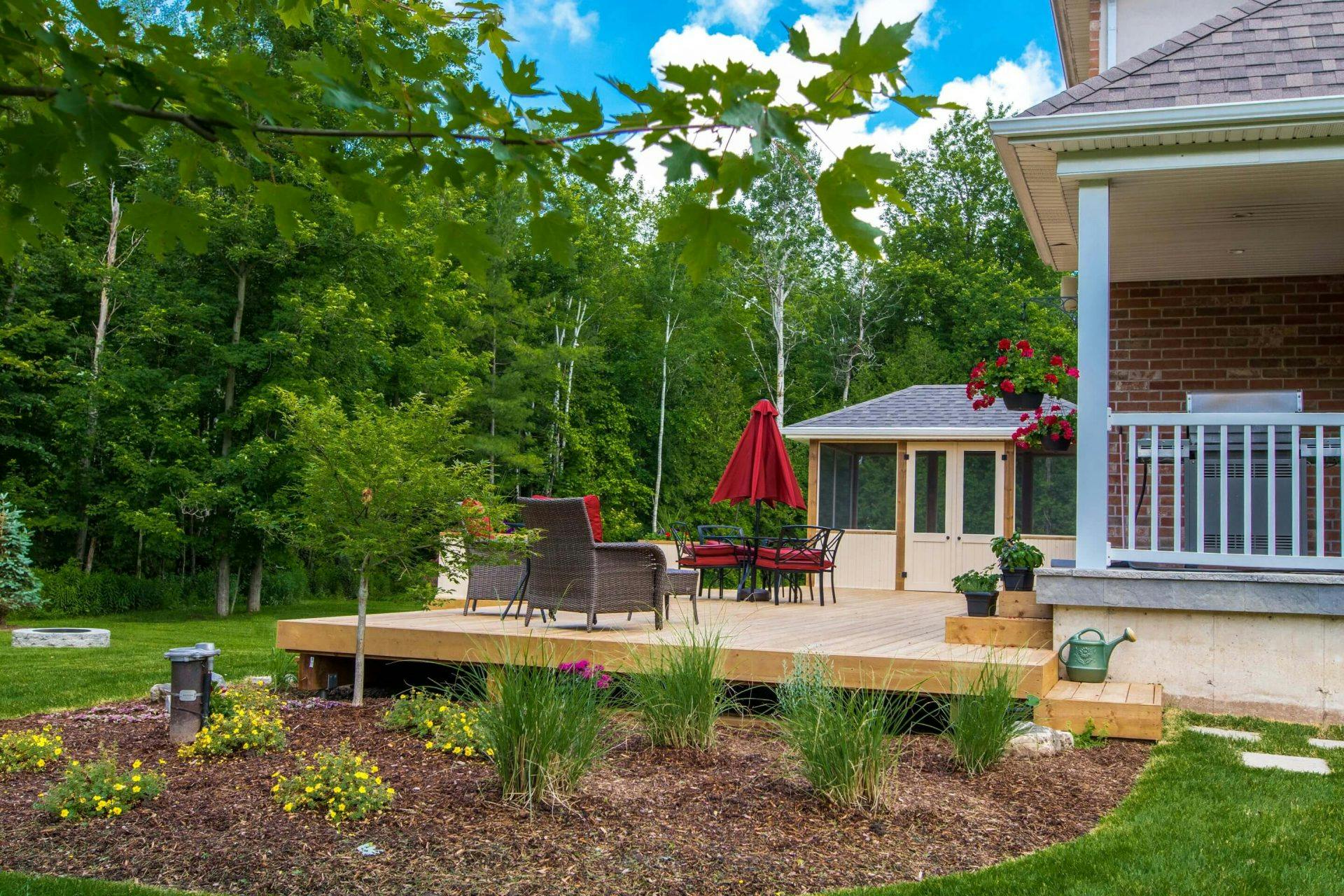 Wooden low backyard deck with beautifully landscaped mulched garden positioned next to it. 