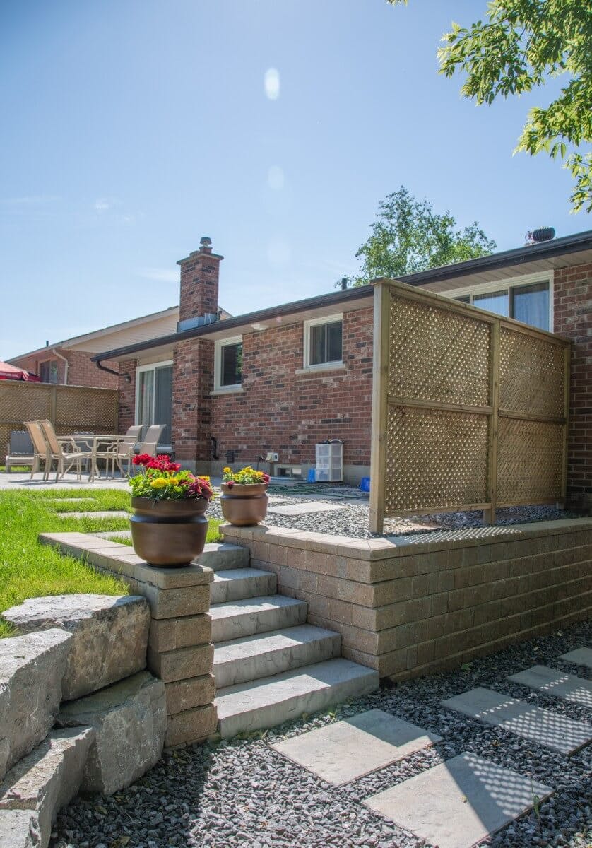 Beautiful four foot retaining wall with wooden privacy screen separating patio backyard from side lot of house. Five stone steps lead from side lot into backyard.  