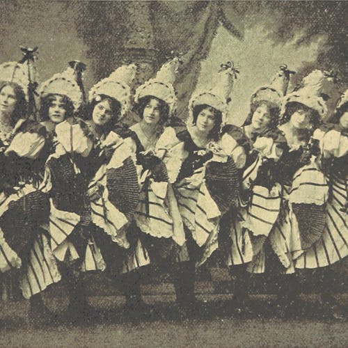 A black-and-white, old-fashioned photo of a chorus line of women wearing full, striped skirts and tall, ribboned hats. 