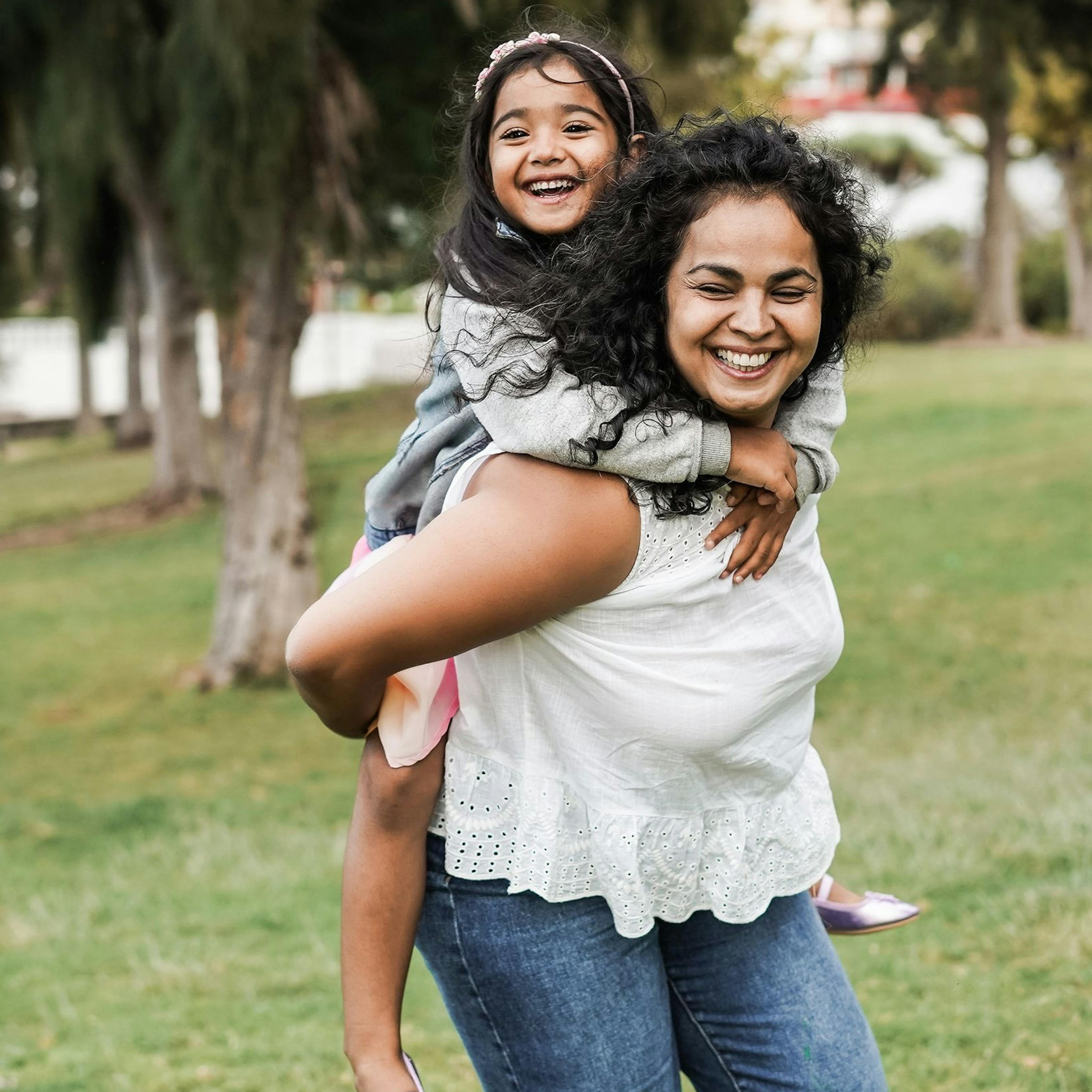 Woman gives smiling daughter a piggyback ride.