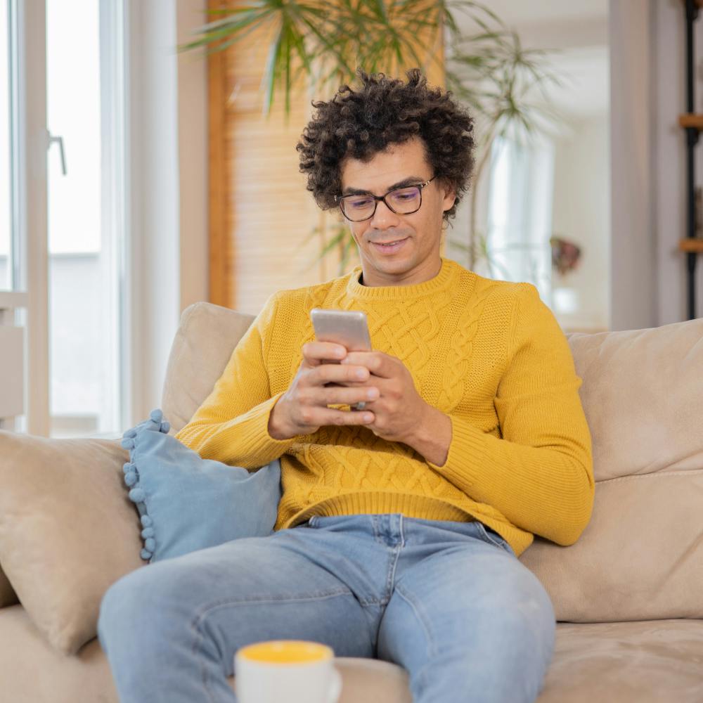 Bespectacled man in a yellow jumper checks his phone.