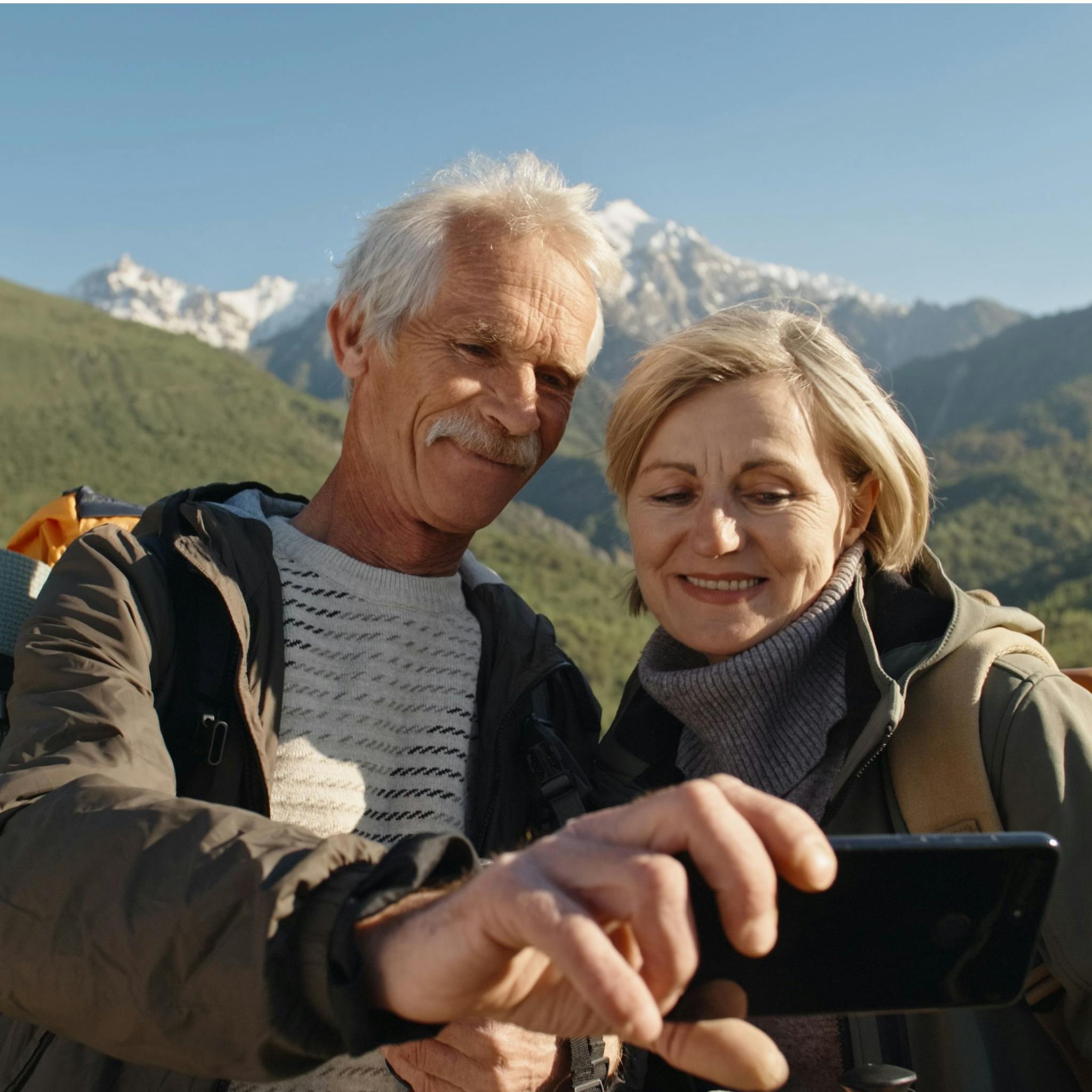 Older couple take selfie with mountain backdrop.