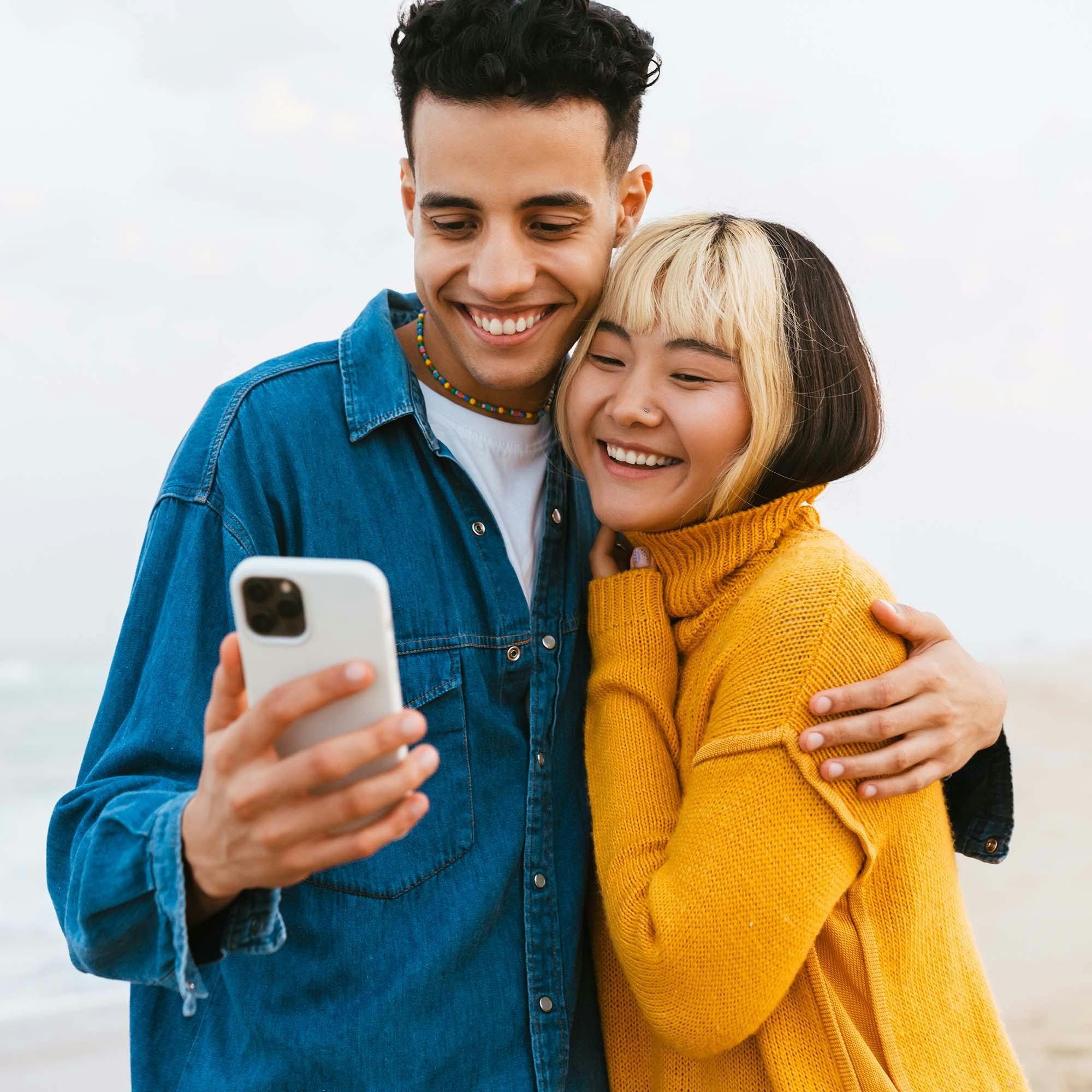 Young couple hug and smile as they take a selfie on a beach