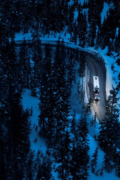 Aerial shot of winding mountain road at night with pine trees and a Keystone Fuzion toy hauler being towed. 