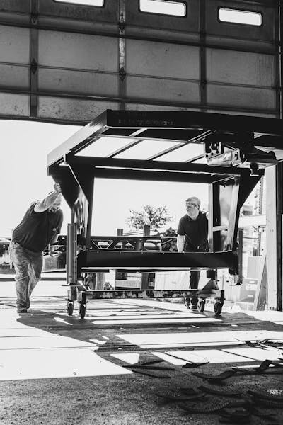 Two men rolling a fifth wheel chassis into a Keystone RV manufacturing plant. 