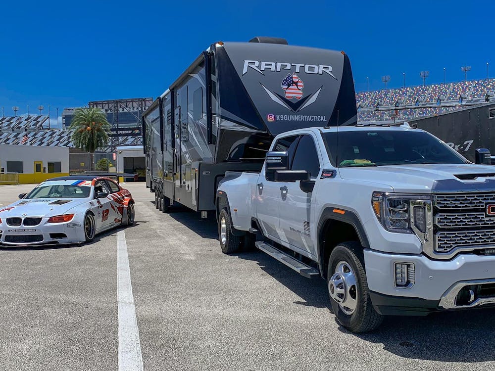 Raptor being hauled by white truck at a racetrack posed by a racecar 