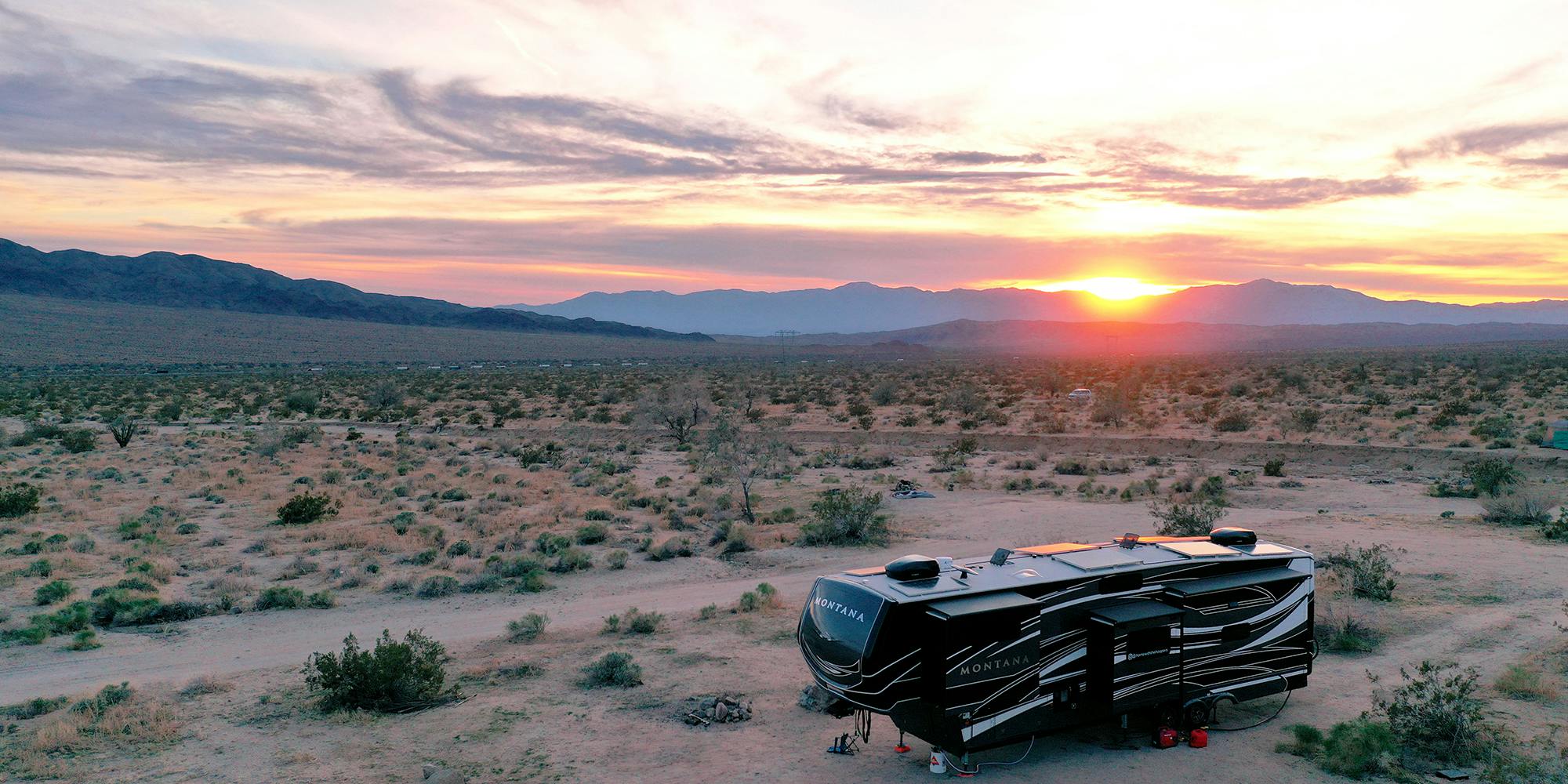 A fifth wheel parked in the desert with a beautiful orange and pink sunset in the background.