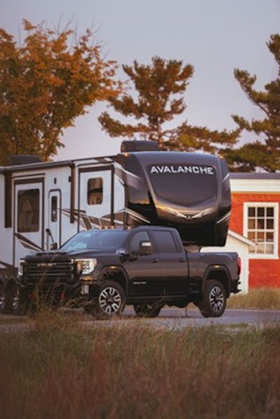 GMC Sierra HD Denali parked at a right angle, pulling a Keystone Avalanche fifth wheel RV. 