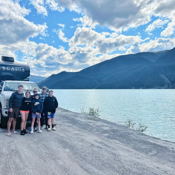 Family standing with Keystone RV in front of Muncho Lake
