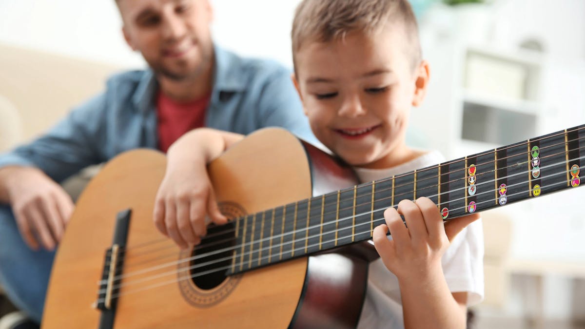 young child placing colourful note stickers on an acoustic guitar fretboard