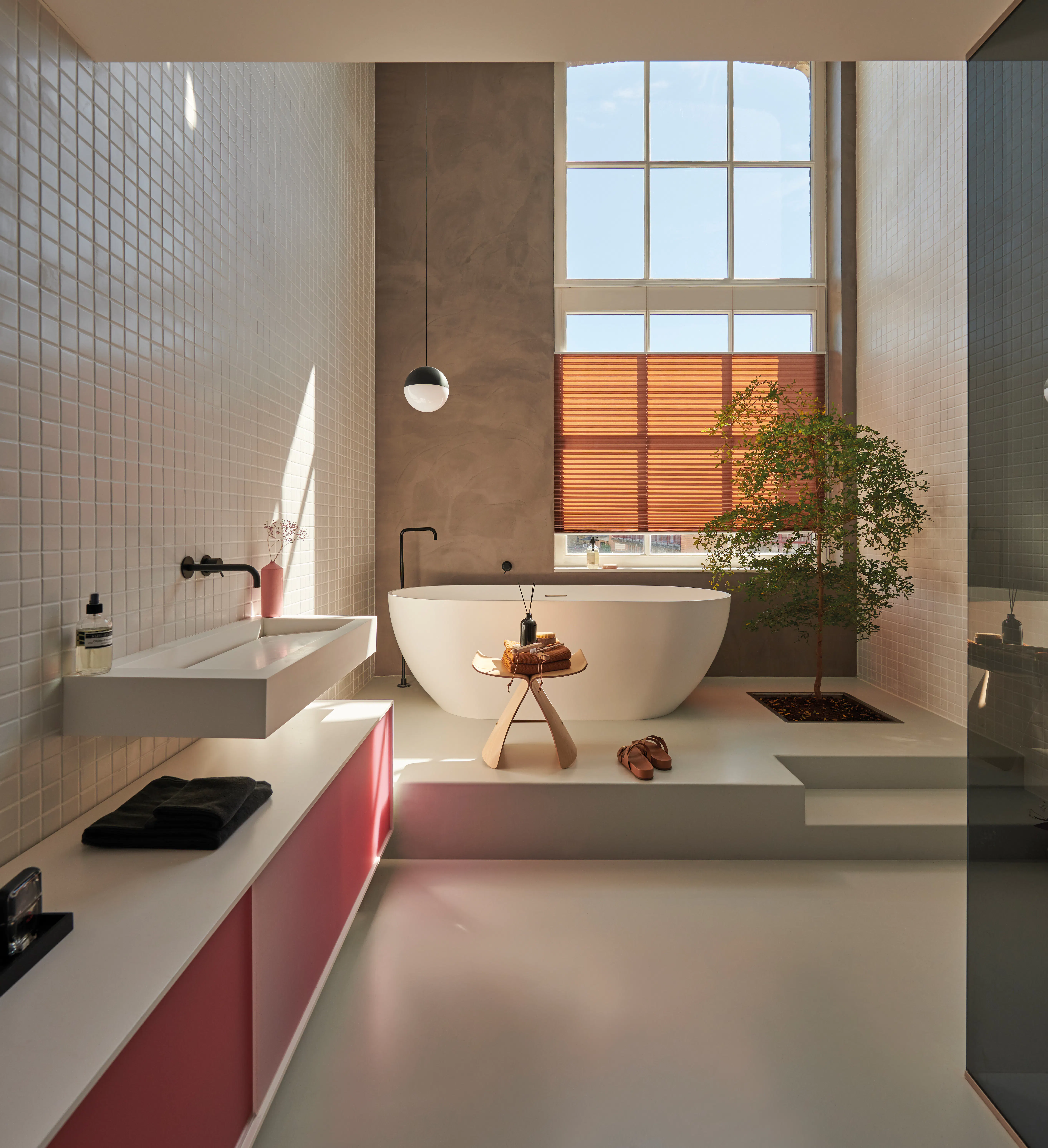 Rullegardin delvis senket, filtrerer dagslys inn i et moderne, lyst stueinteriør med sofa, salongbord, plante og tregulv foran et stort vindu.