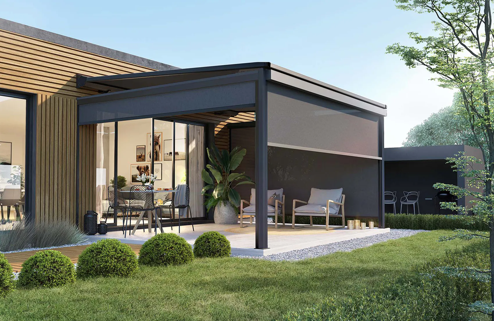 En moderne pergola med nedrullet solskjerm/sidegardin skaper skygge over en møblert terrasse. Den er festet til en trekledd enebolig, omgitt av pyntebusker, gressplen og hage.