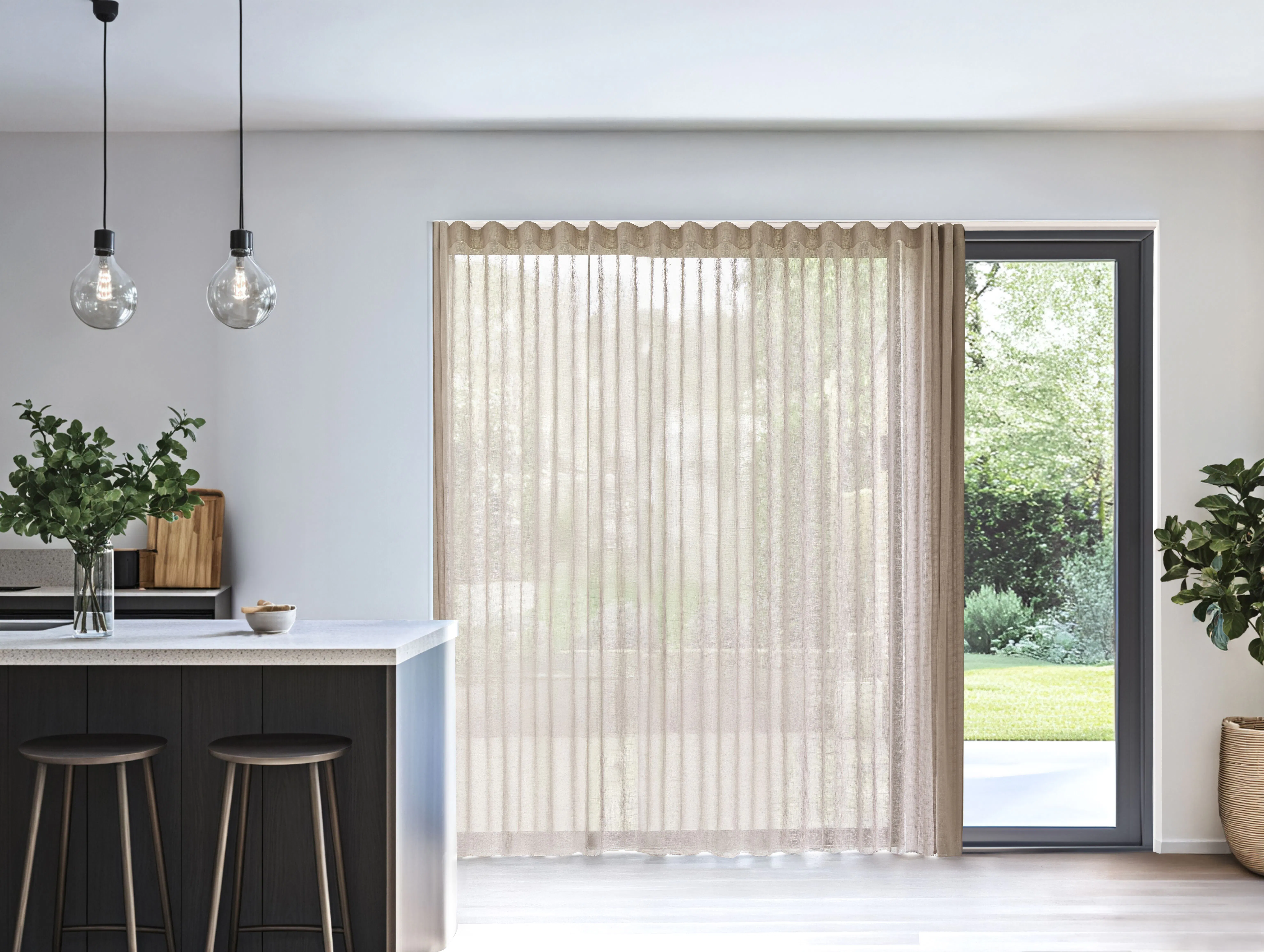 Lyst kjøkken med beige, transparente gardiner foran et stort vindu og en glassdør ut mot hagen.