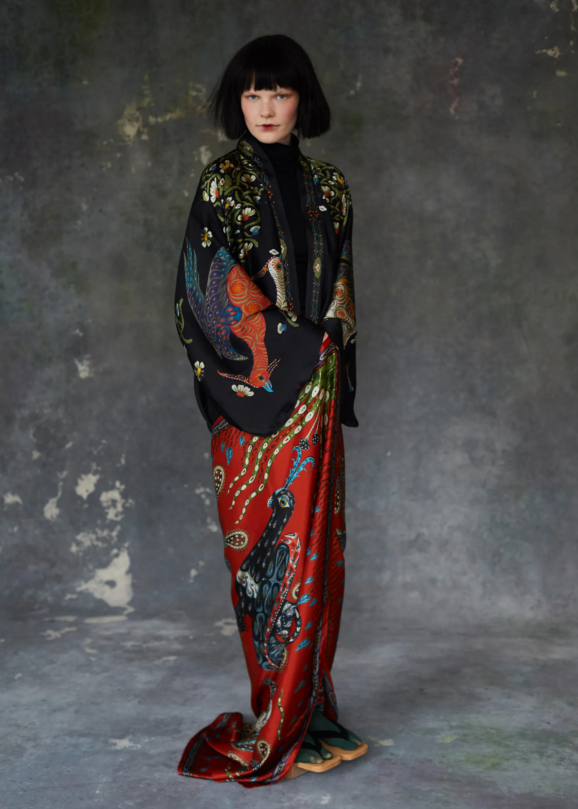 Woman in a black Firebird kimono with a red Firebird silk scarf, against a grey plaster wall