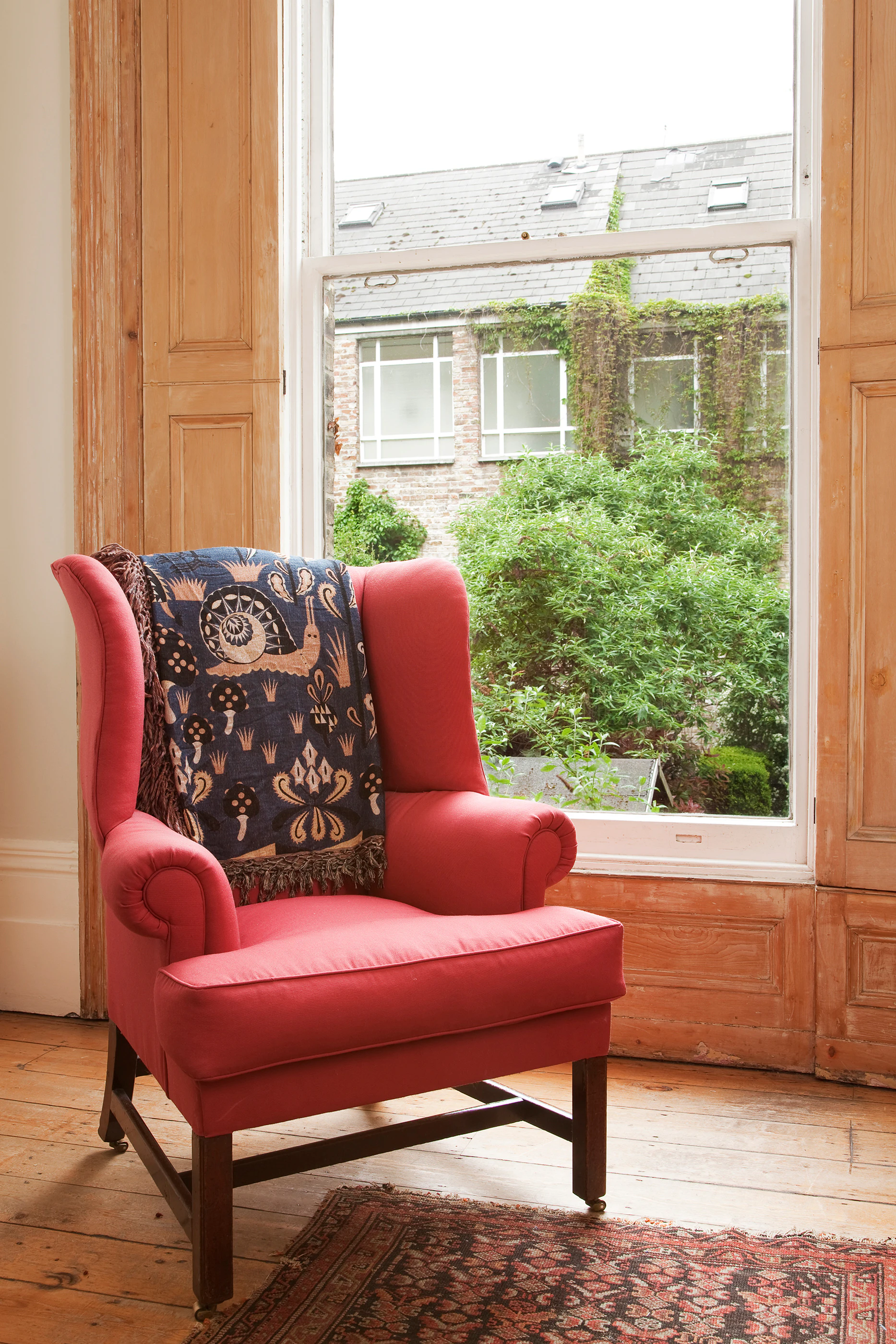 Klaus Haapaniemi bird throw draped over a red wingback armchair by a tall window