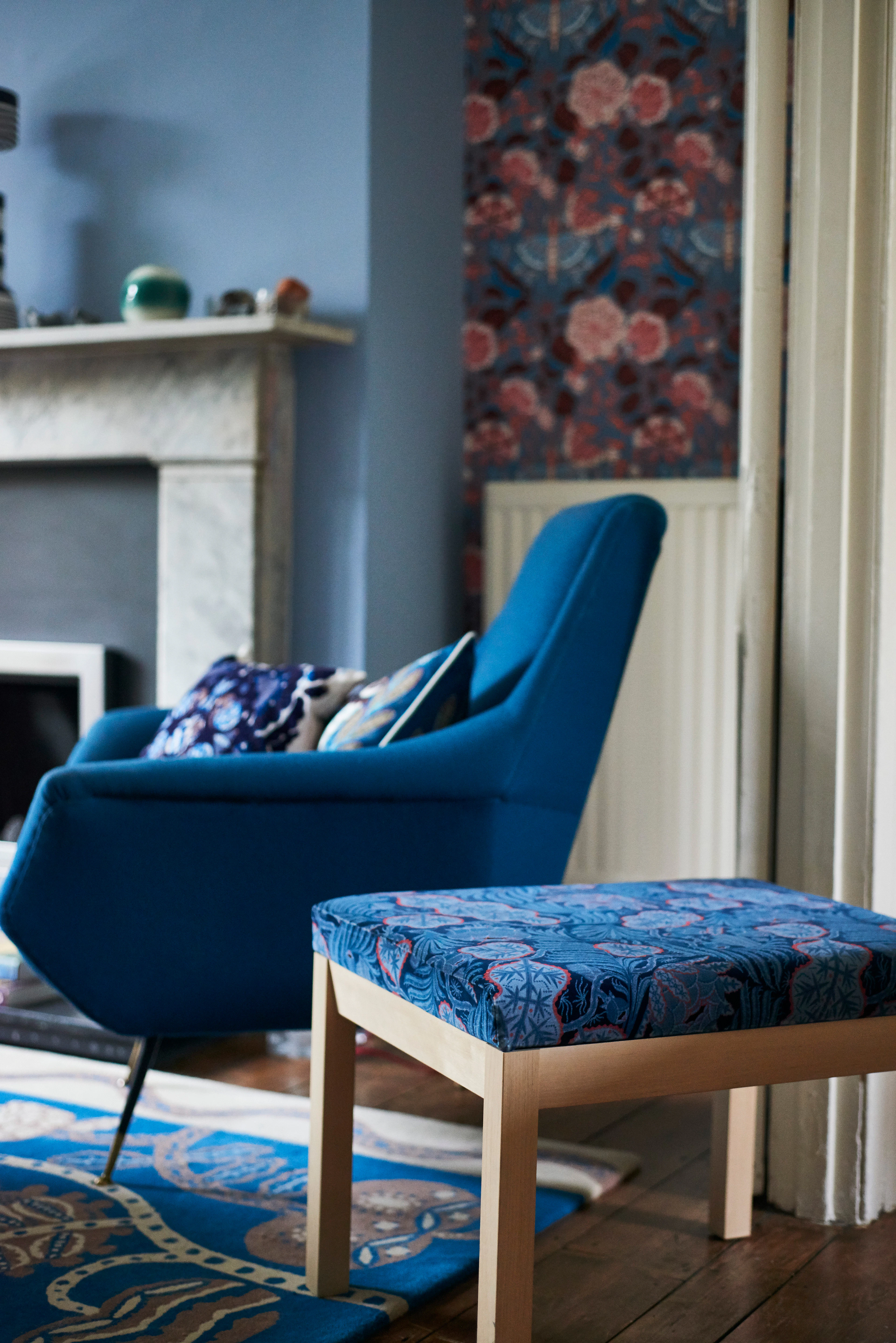 Blue armchair with printed cushions beside a footstool upholstered in Iceflower blue velvet