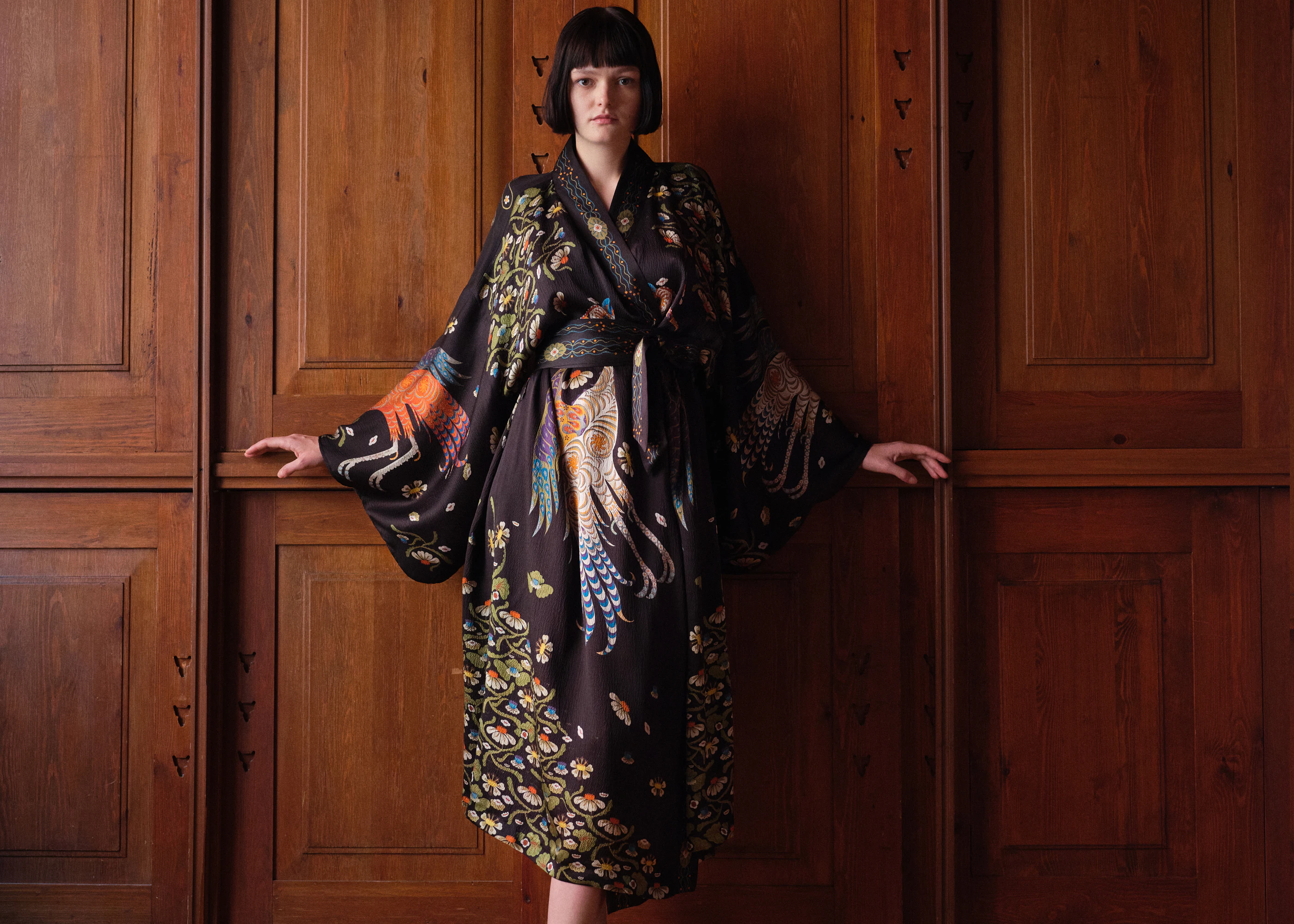Woman in the long Firebird kimono belted at the waist as a dress, against wooden panelling