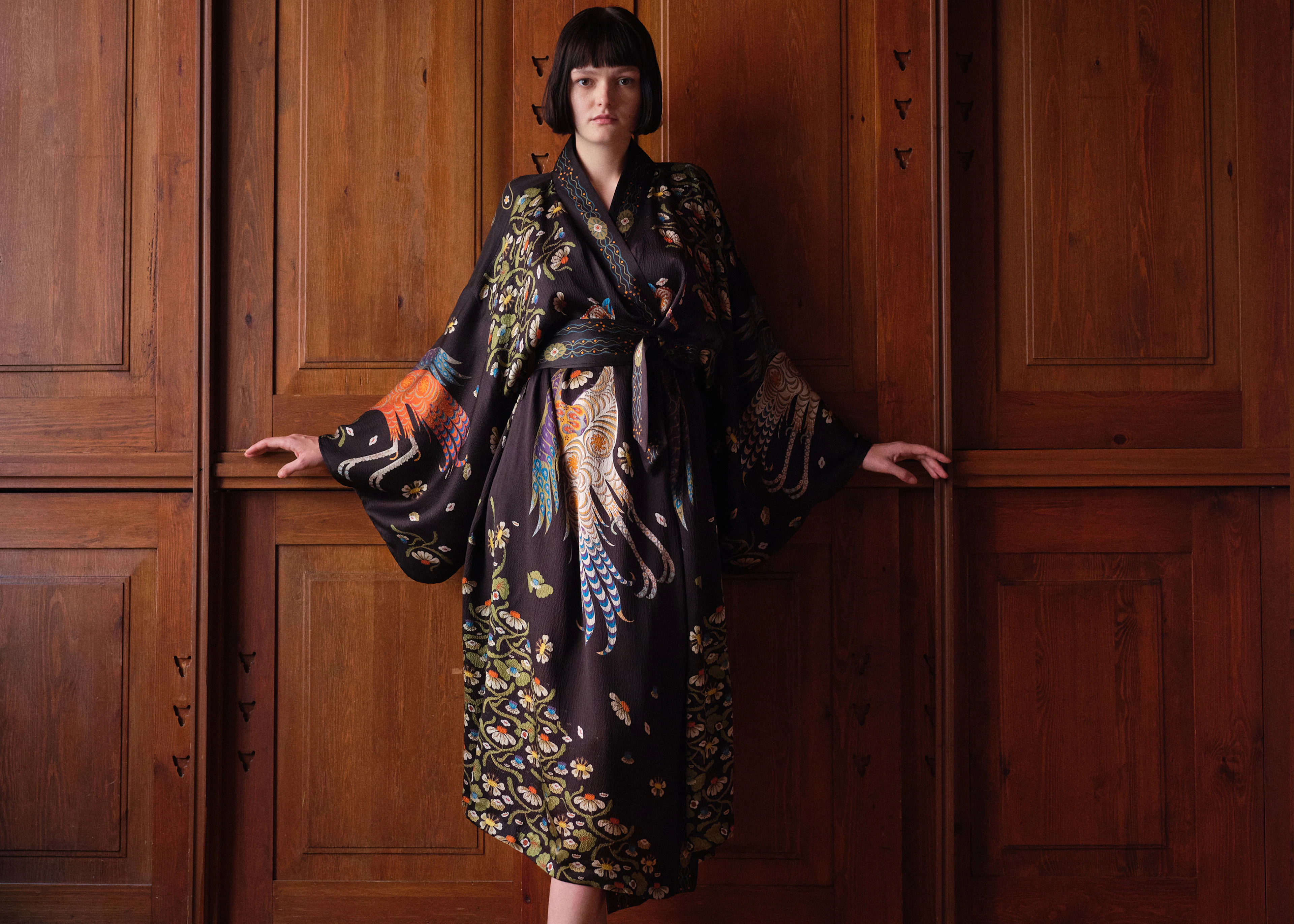 Woman in the long Firebird kimono belted at the waist as a dress, against wooden panelling