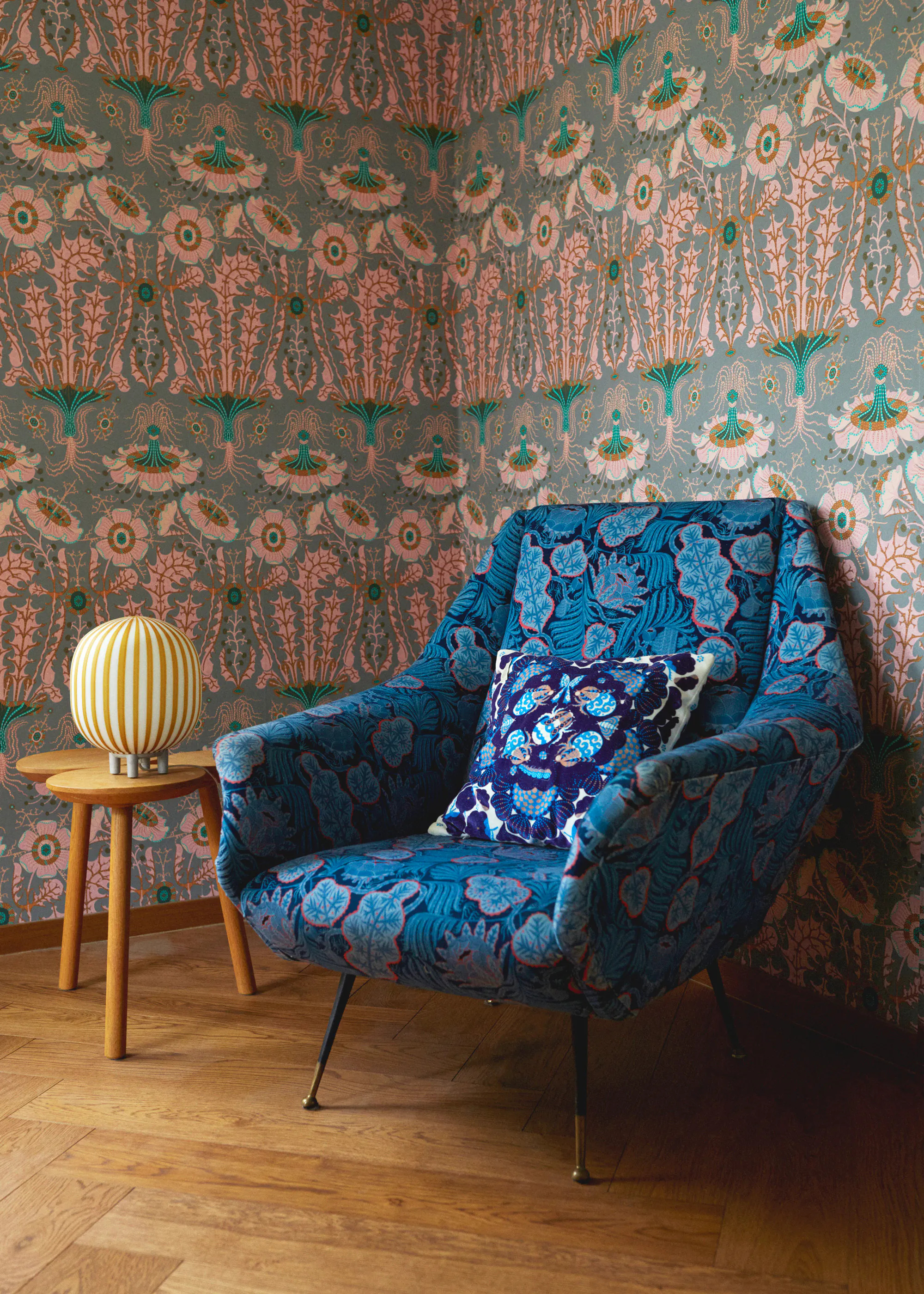 Equinoxe wallpaper by Klaus Haapaniemi with a blue patterned armchair, a printed cushion and a small table lamp