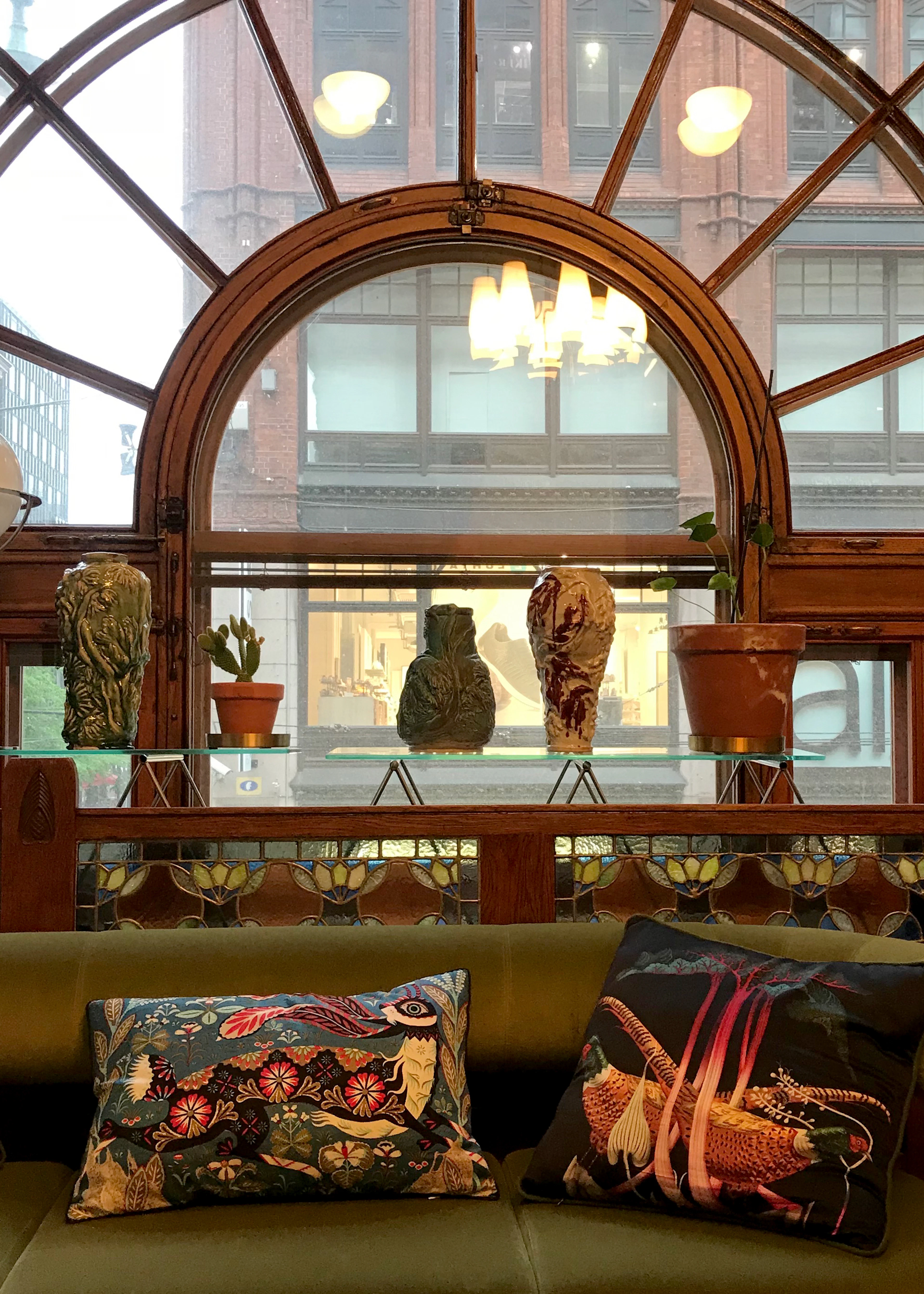 Printed Klaus Haapaniemi cushions on a green sofa beneath an arched window