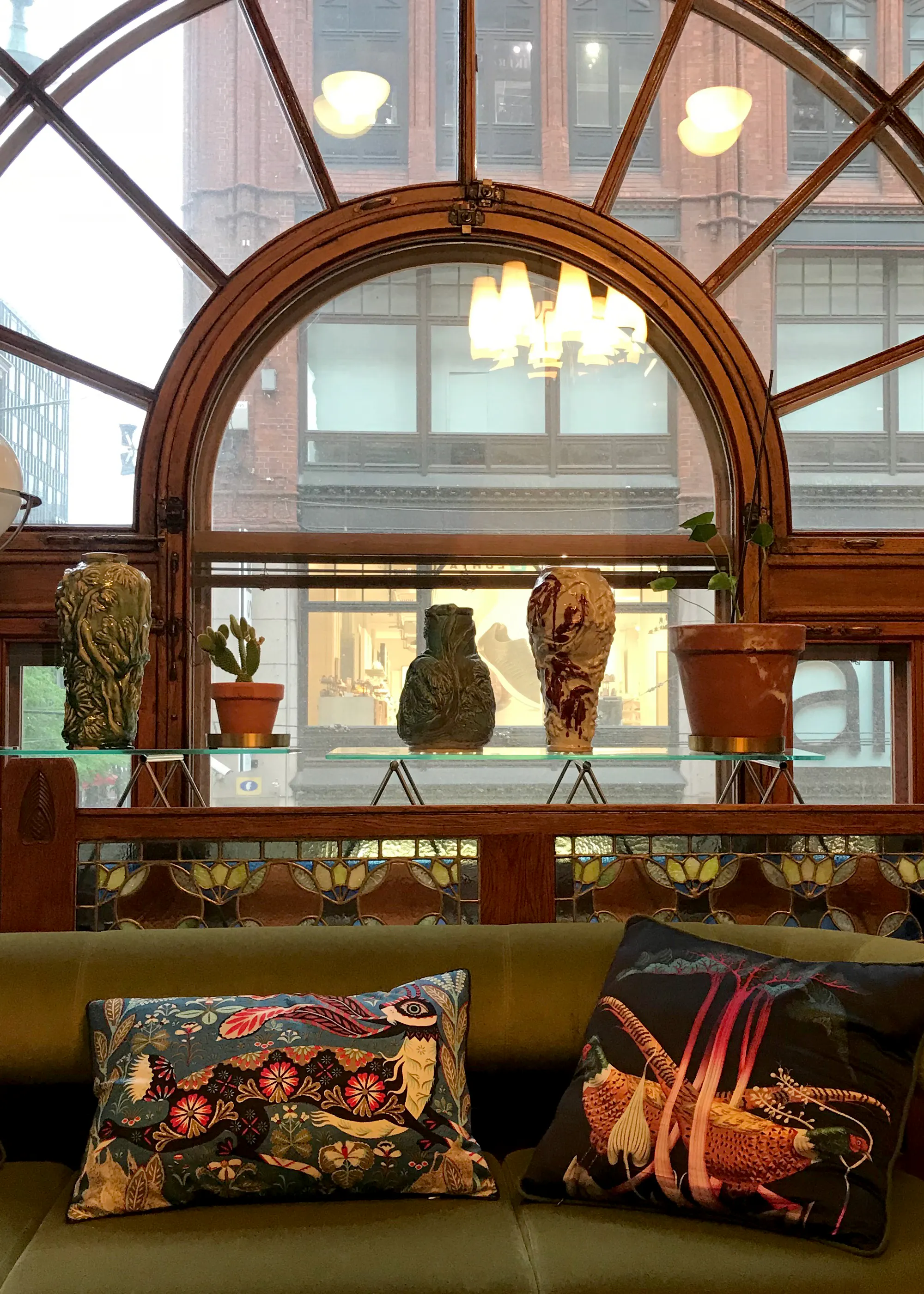 Printed Klaus Haapaniemi cushions on a green sofa beneath an arched window