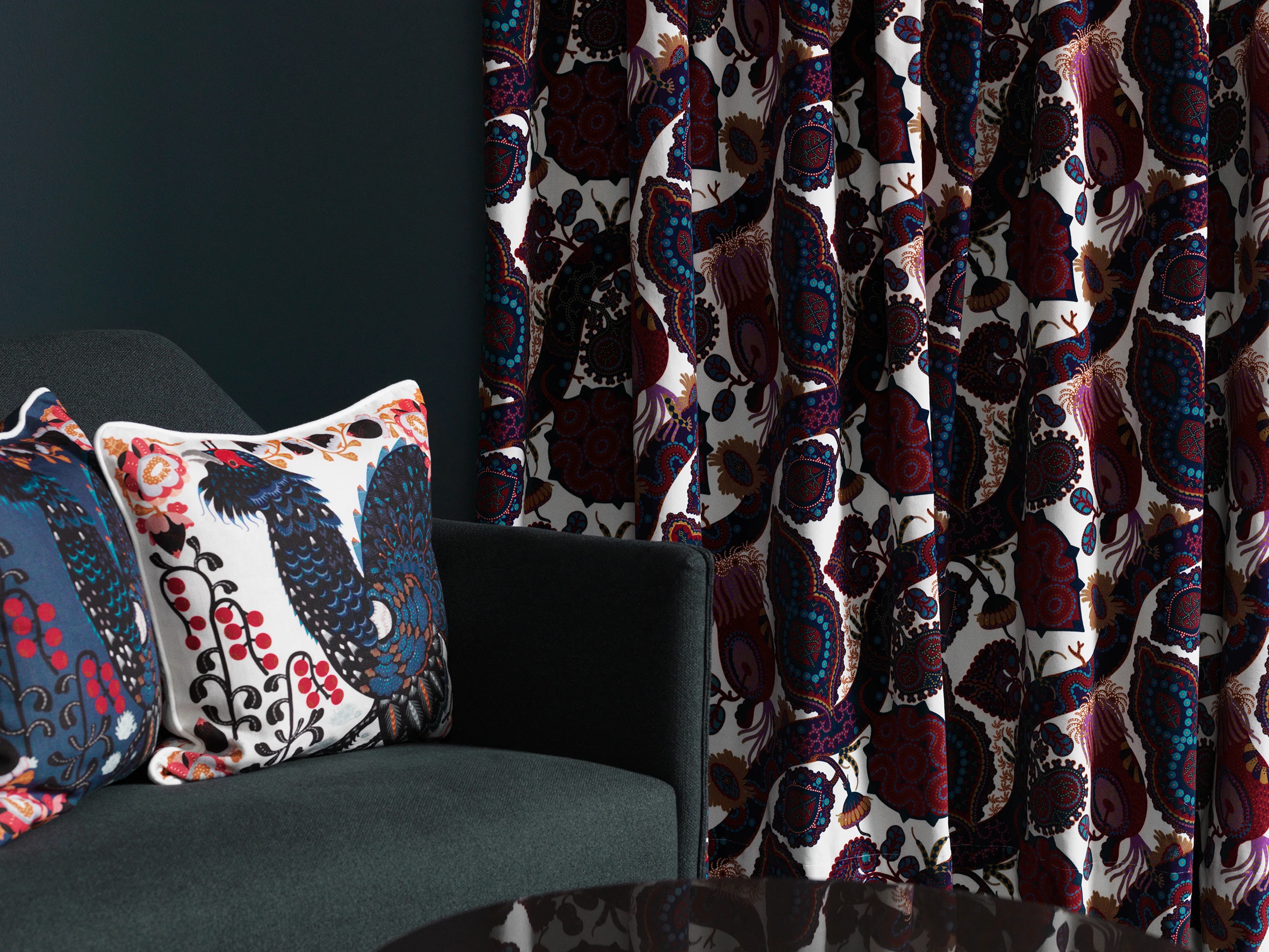 Printed Klaus Haapaniemi cushions with birds and berries on a grey armchair beside Purple Rain velvet curtains