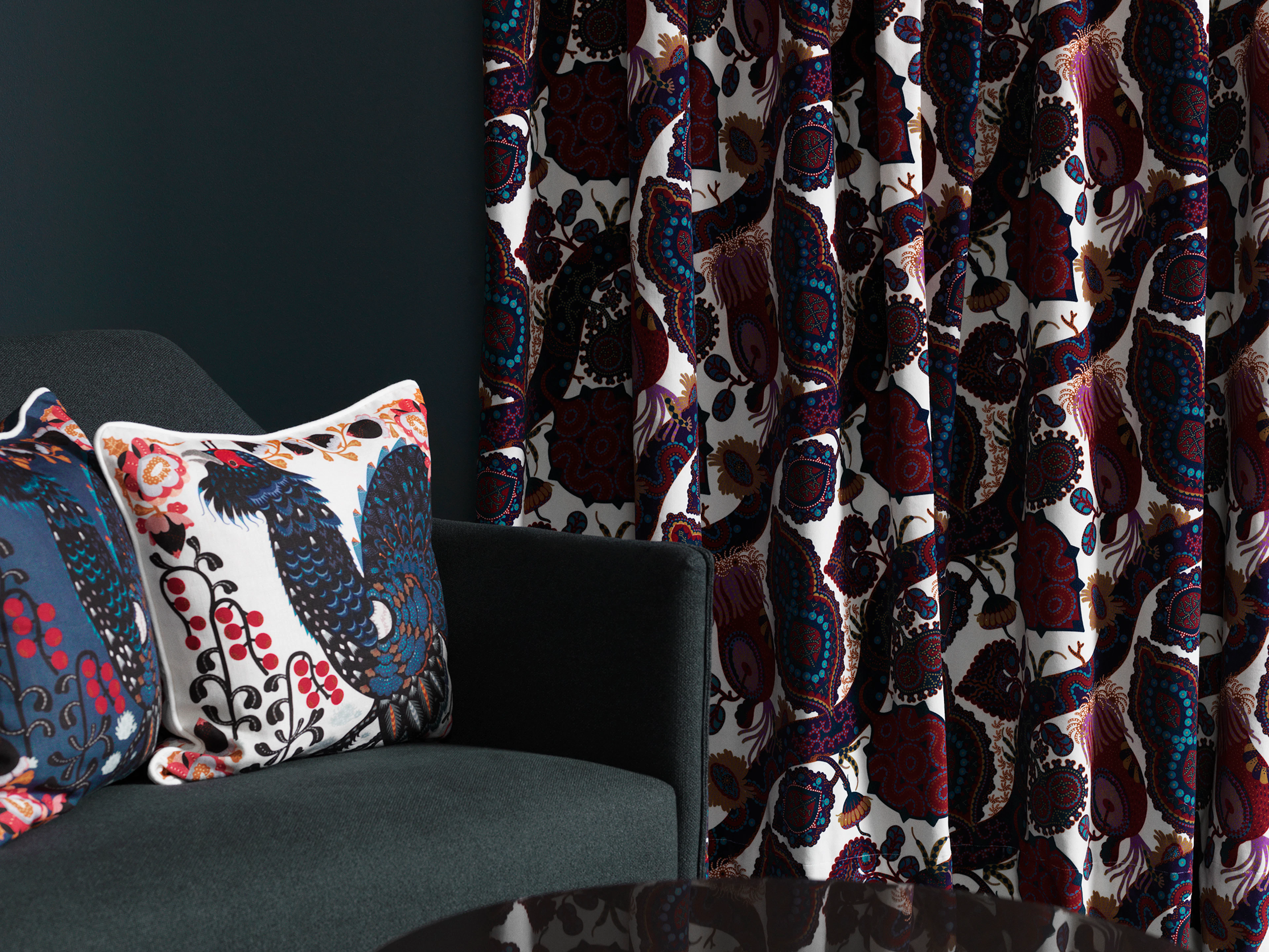 Printed Klaus Haapaniemi cushions with birds and berries on a grey armchair beside Purple Rain velvet curtains
