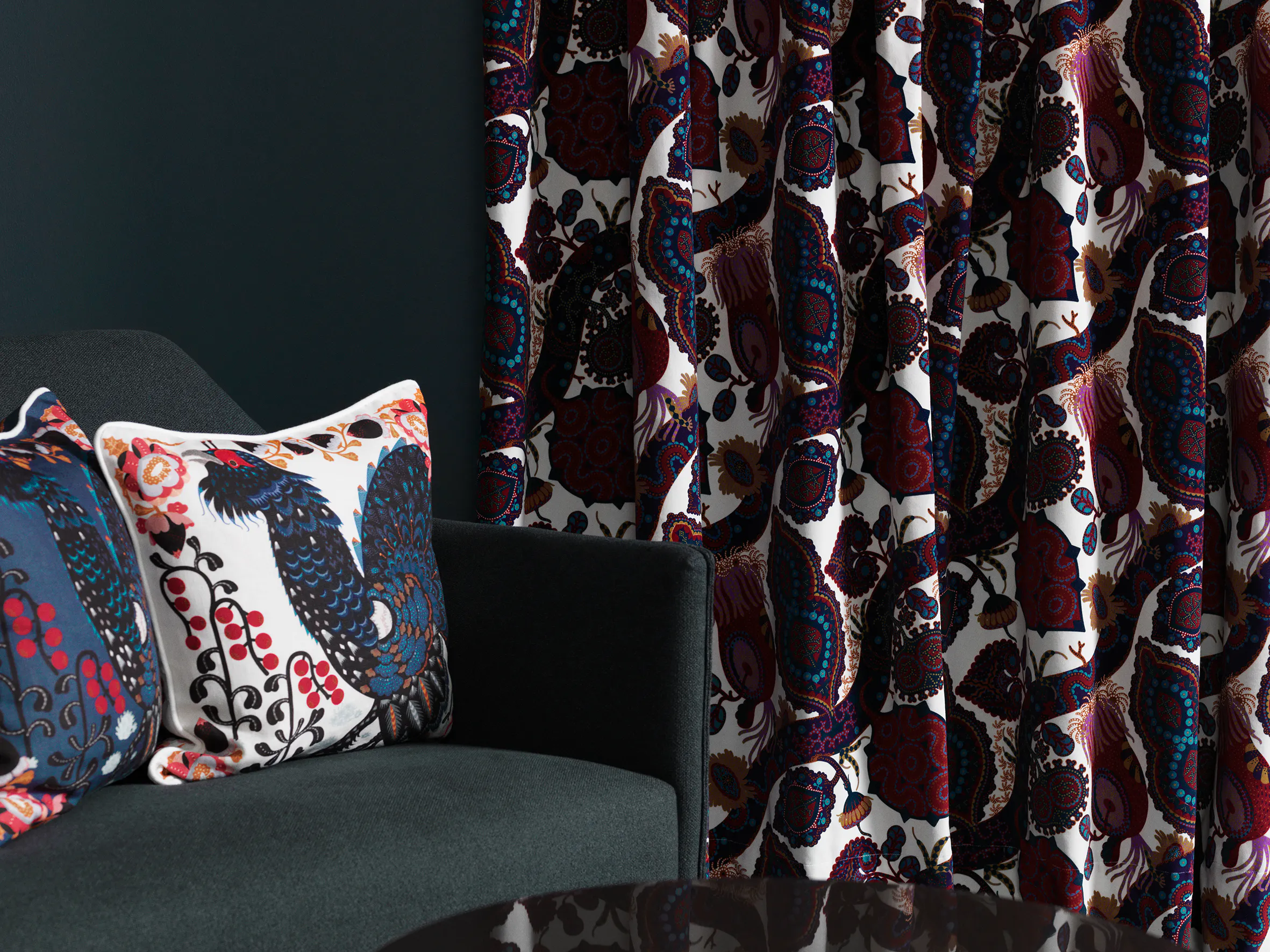 Printed Klaus Haapaniemi cushions with birds and berries on a grey armchair beside Purple Rain velvet curtains