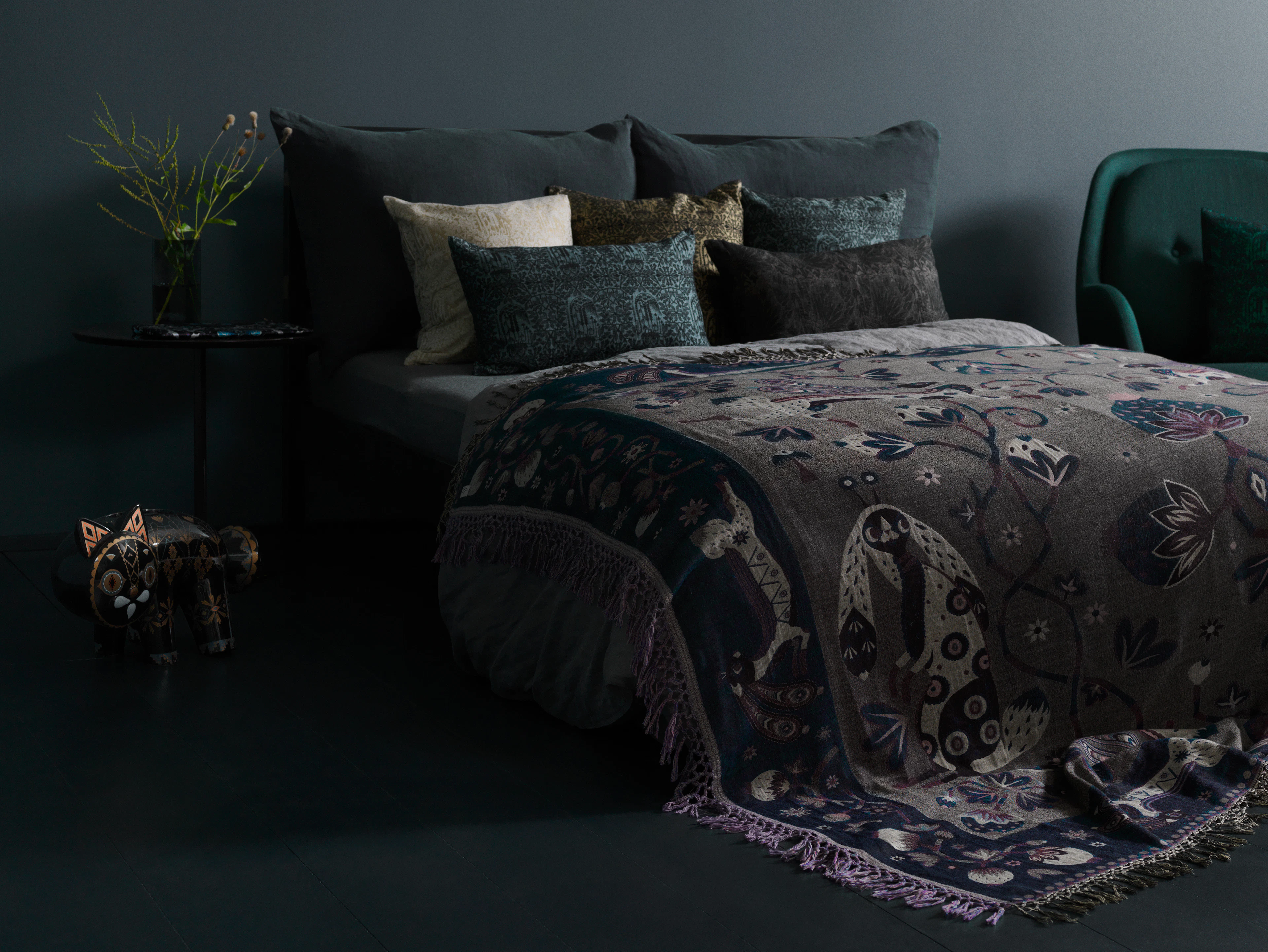 Dark bedroom with a patterned Klaus Haapaniemi throw layered over the bed and printed cushions