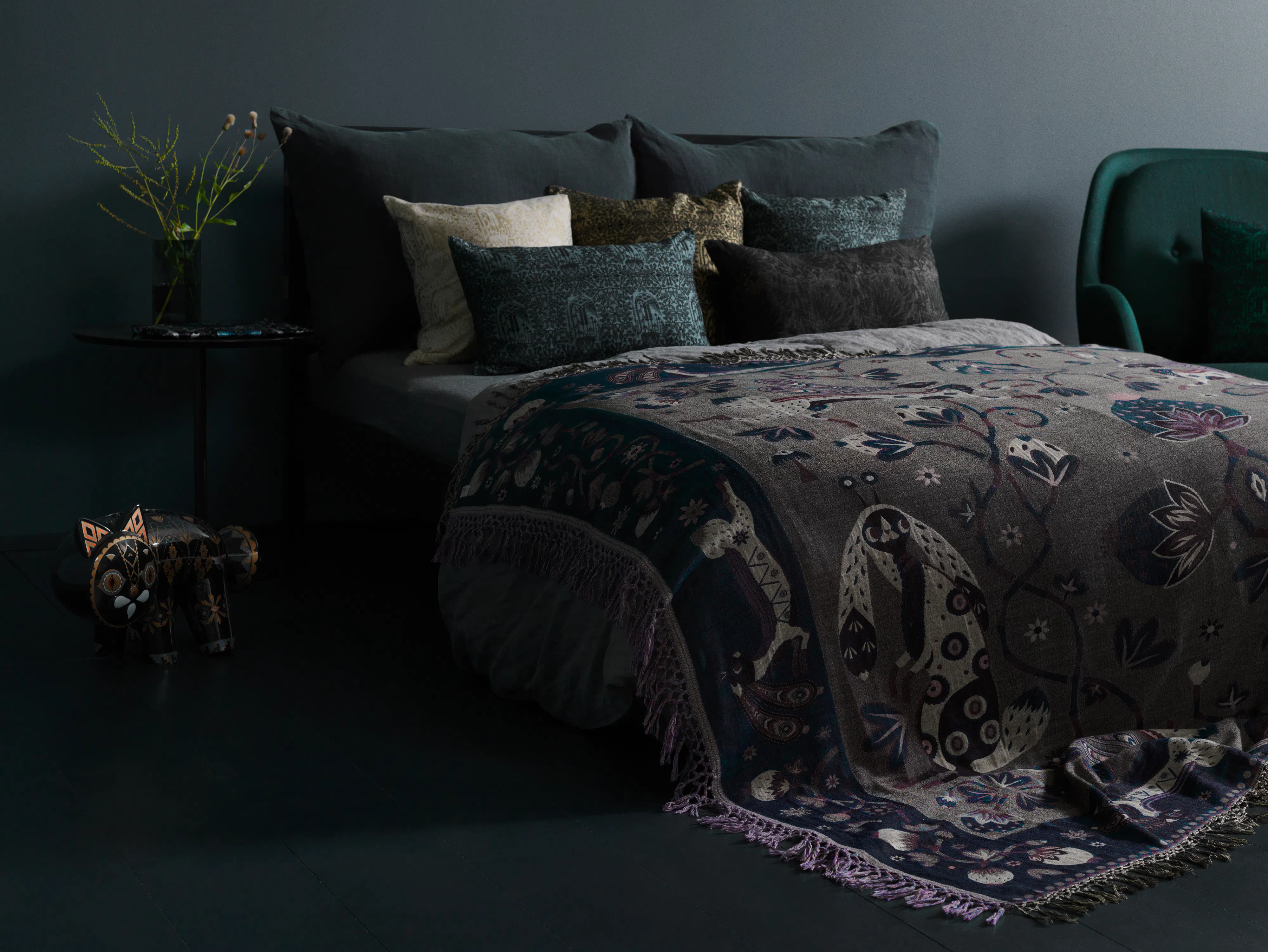 Dark bedroom with a patterned Klaus Haapaniemi throw layered over the bed and printed cushions