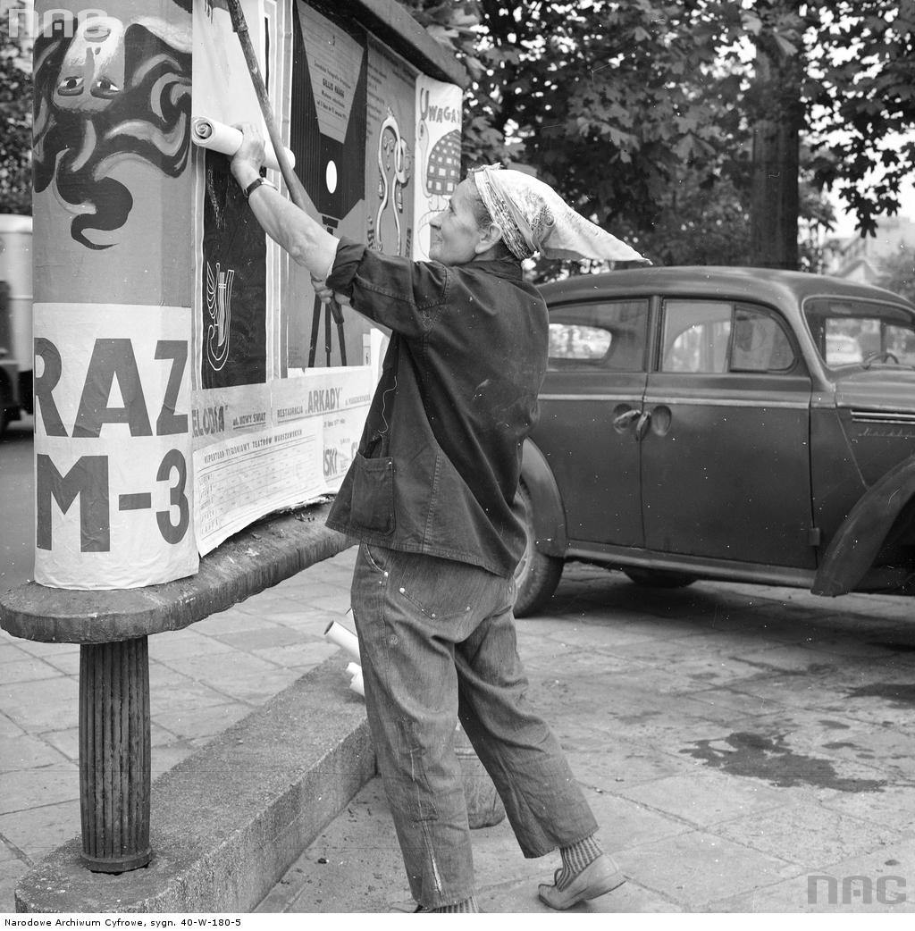 A woman pasting a poster onto a wall in Warsaw, 1971. Public domain