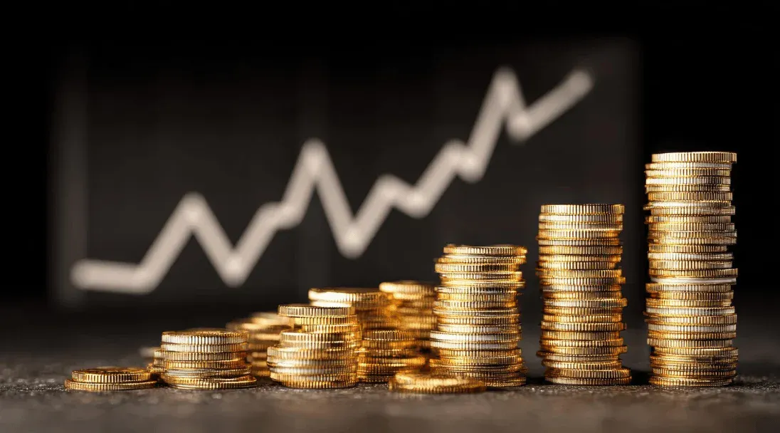 Pilha de moedas de ouro formando uma pirâmide de crescimento com gráfico ascendente ao fundo, simbolizando aumento de receita e investimento financeiro.