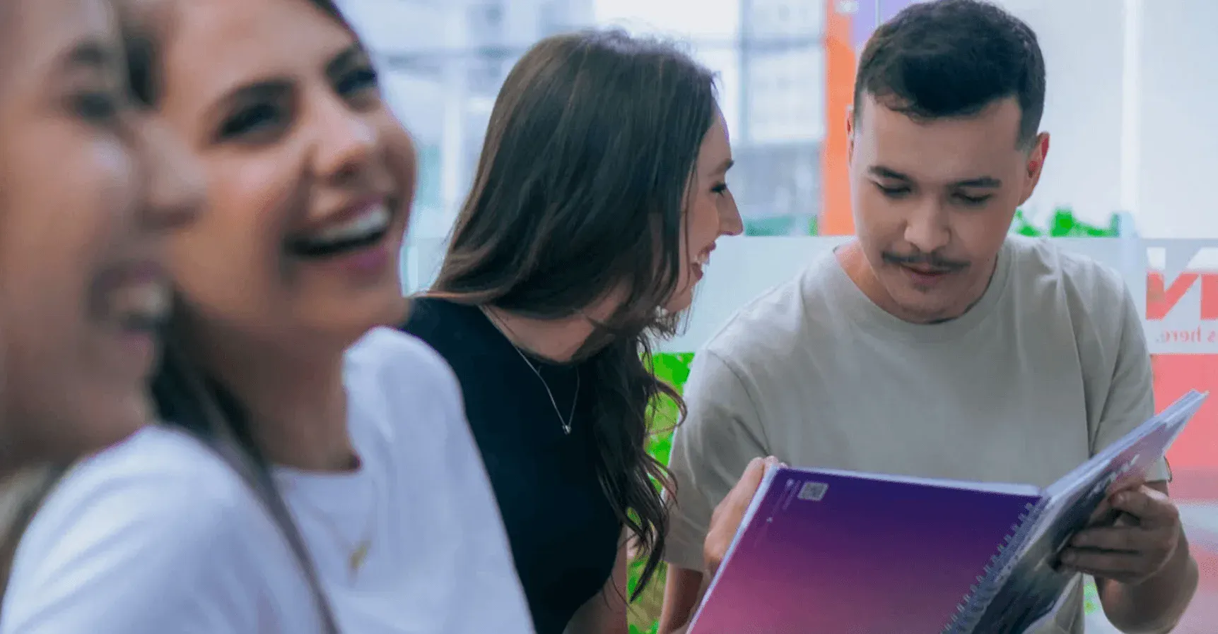 Equipe em ambiente corporativo lendo um catálogo e discutindo ideias, com duas pessoas ao centro olhando para um material impresso em uma sala com fundo desfocado.