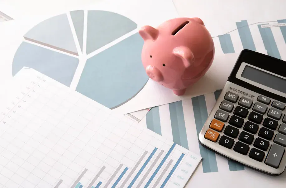 Cofrinho rosa sobre gráficos e relatórios financeiros, com calculadora ao lado, sugerindo planejamento orçamentário e controle de gastos em uma mesa de trabalho.