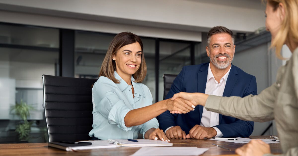 Um homem e uma mulher apertando as mãos durante uma reunião, simbolizando um acordo ou colaboração profissional.