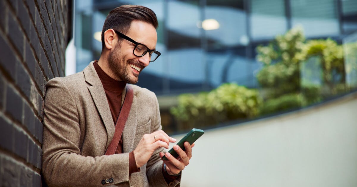 Um homem de óculos observa atentamente seu telefone celular.