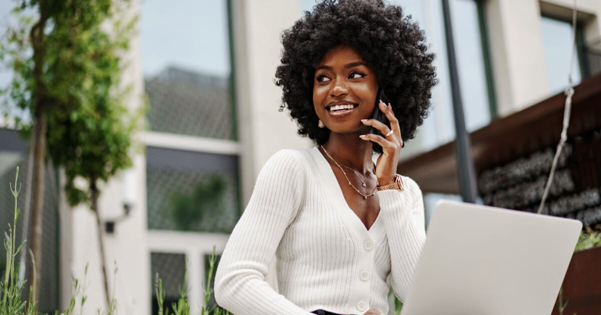 Uma mulher com um laptop e falando no celular, concentrada em seu trabalho.