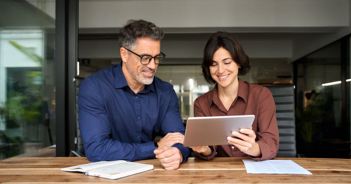 Um homem e uma mulher observam atentamente um tablet, compartilhando informações e interagindo com a tela.