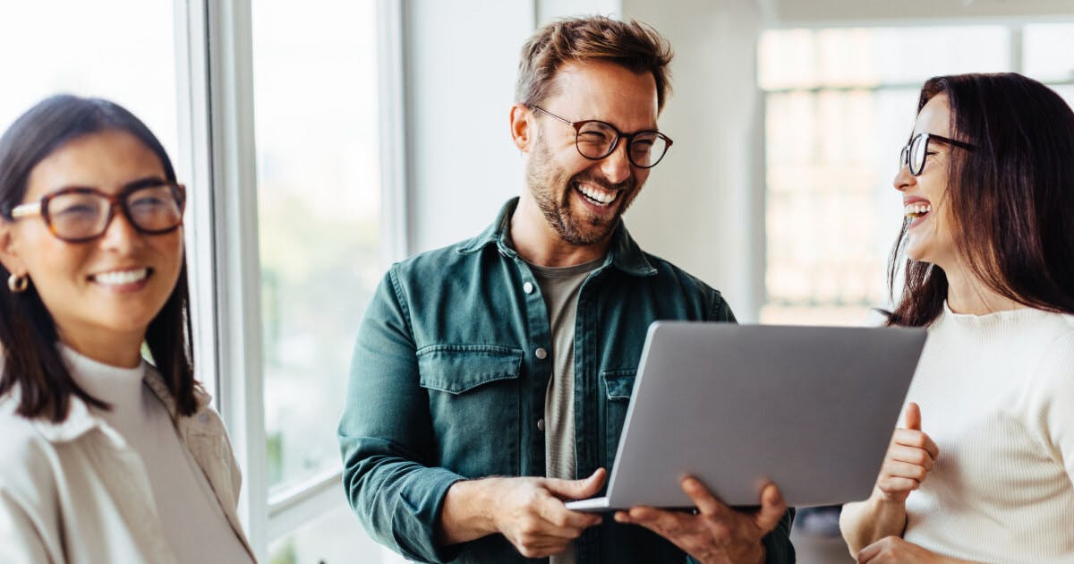 Duas mulheres e um homem sorrindo e olhando um computador