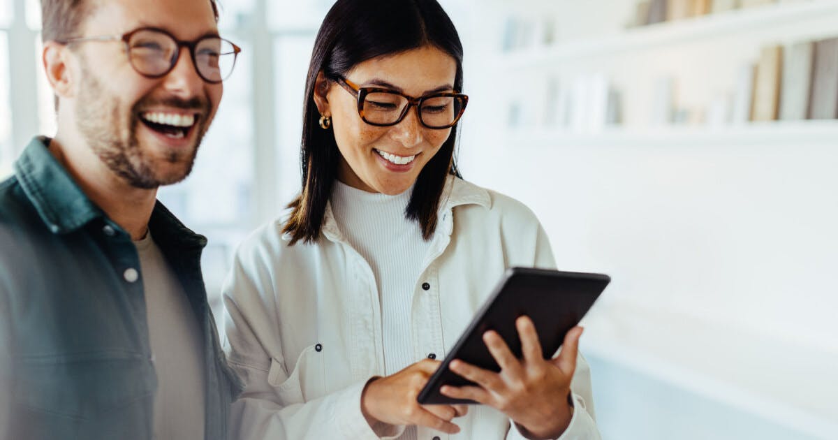 Um casal empreendedor sorrindo e alegre. Os dois estão de óculos e ela está com um tablet na mão.