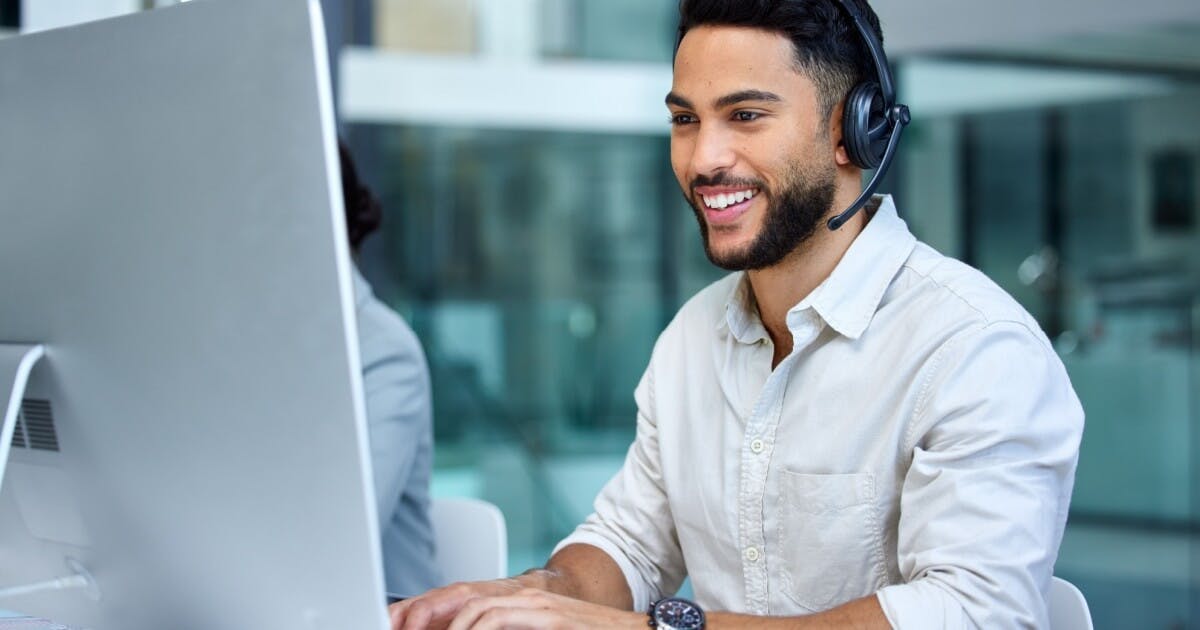 Um homem com headseat sorrindo em frente a um computador