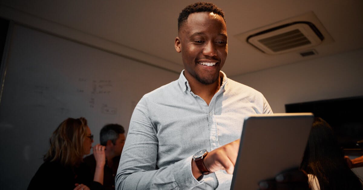 Homem sorridente utilizando um computador portátil, demonstrando satisfação e concentração em sua atividade.