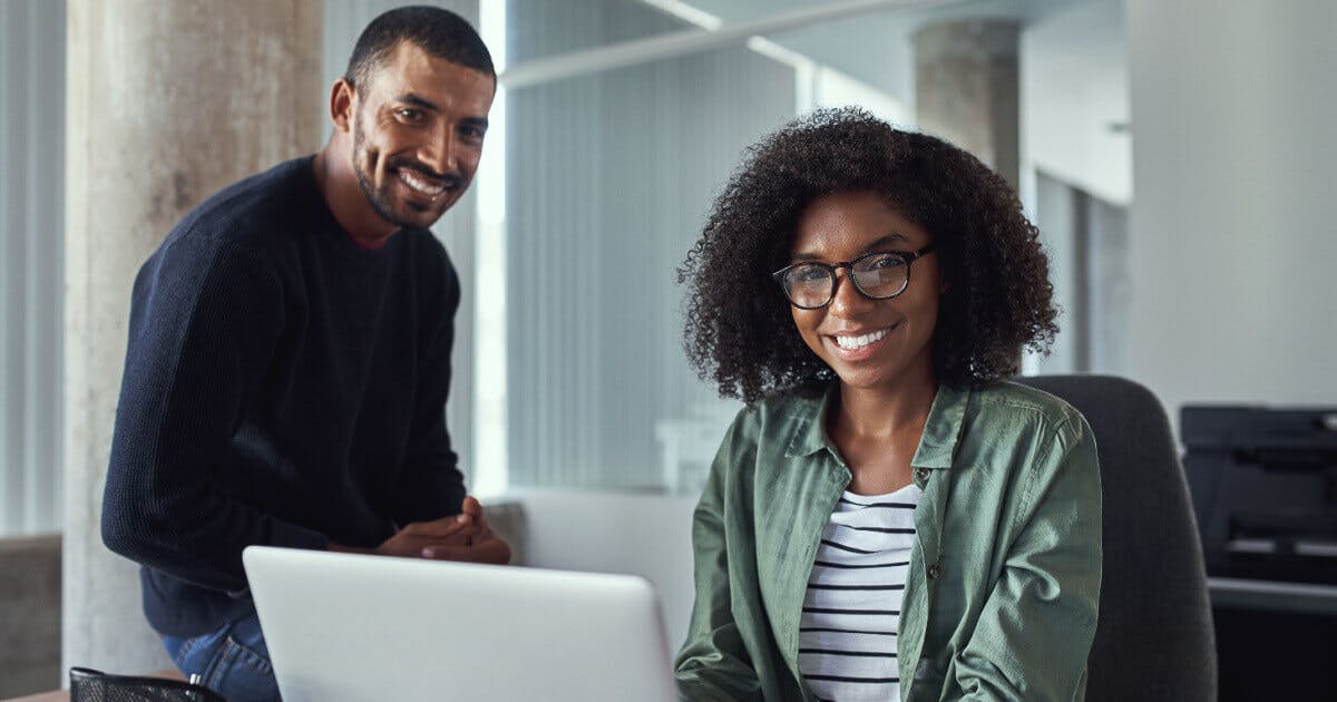 Homem e mulher sorridentes sentados à mesa com um laptop, transmitindo um ambiente de colaboração e alegria.