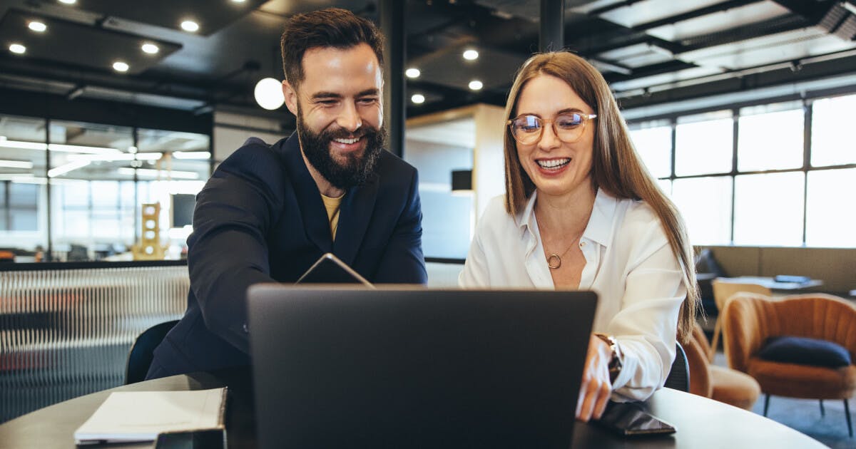 Homem e mulher sorrindo enquanto observam um laptop, transmitindo alegria e colaboração em um ambiente digital.